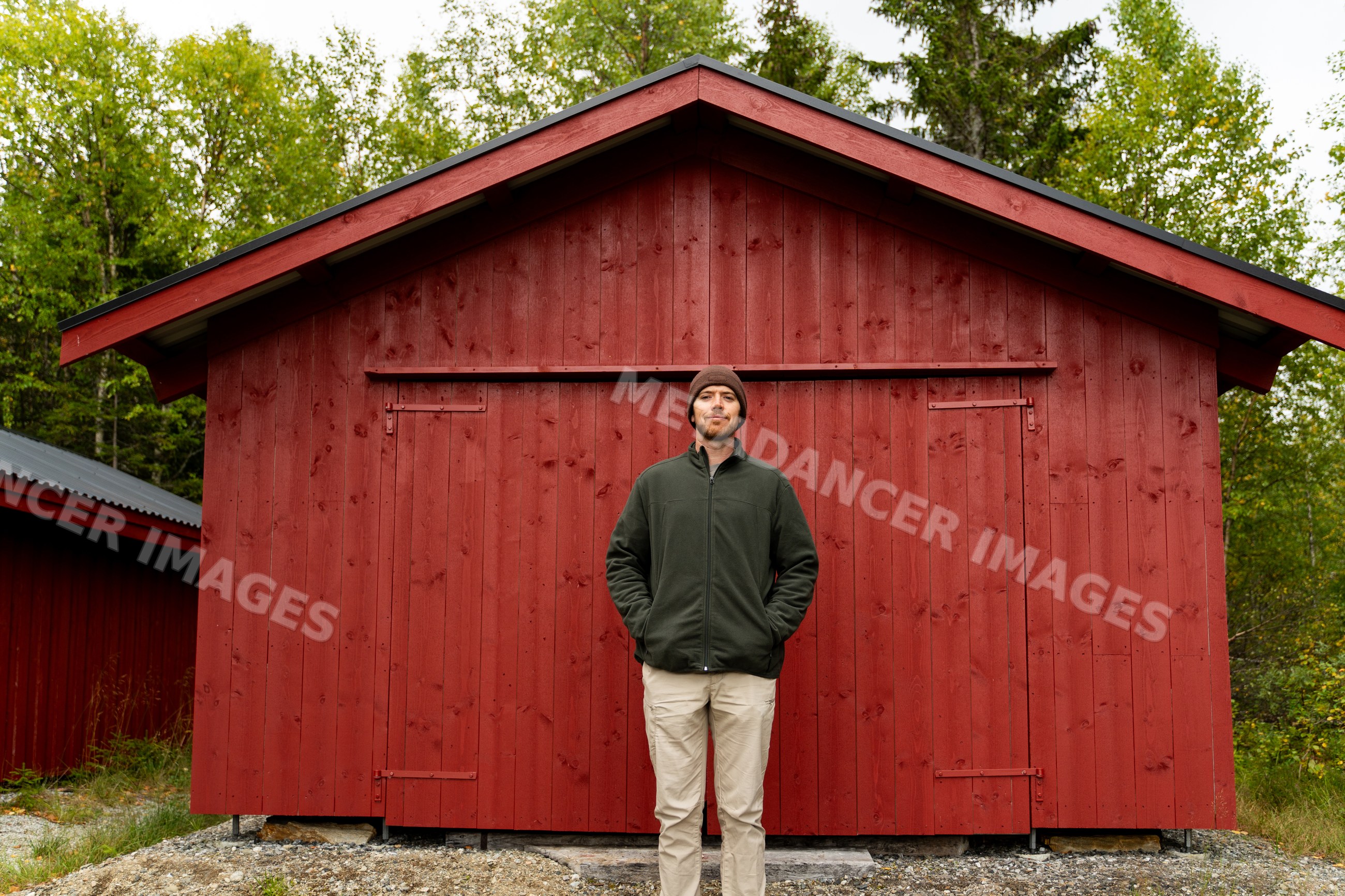 Man standing in front of red wooden cabin in norwegian forest