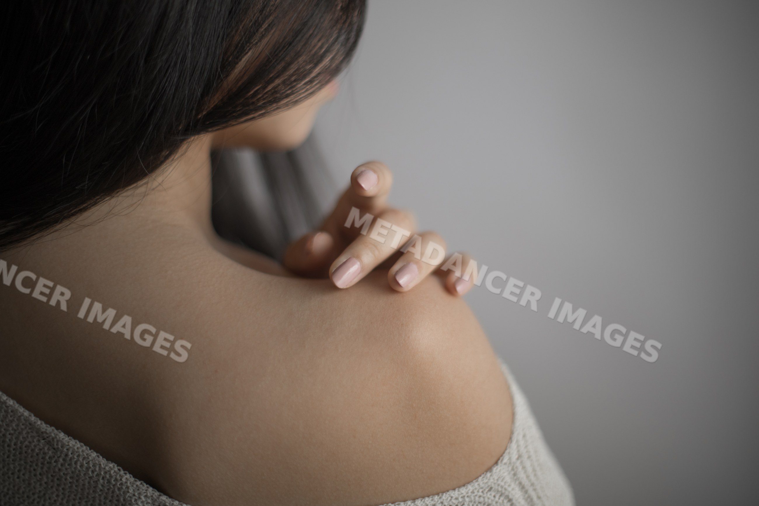 Southeast Asian woman touching her bare shoulder with gentle hand