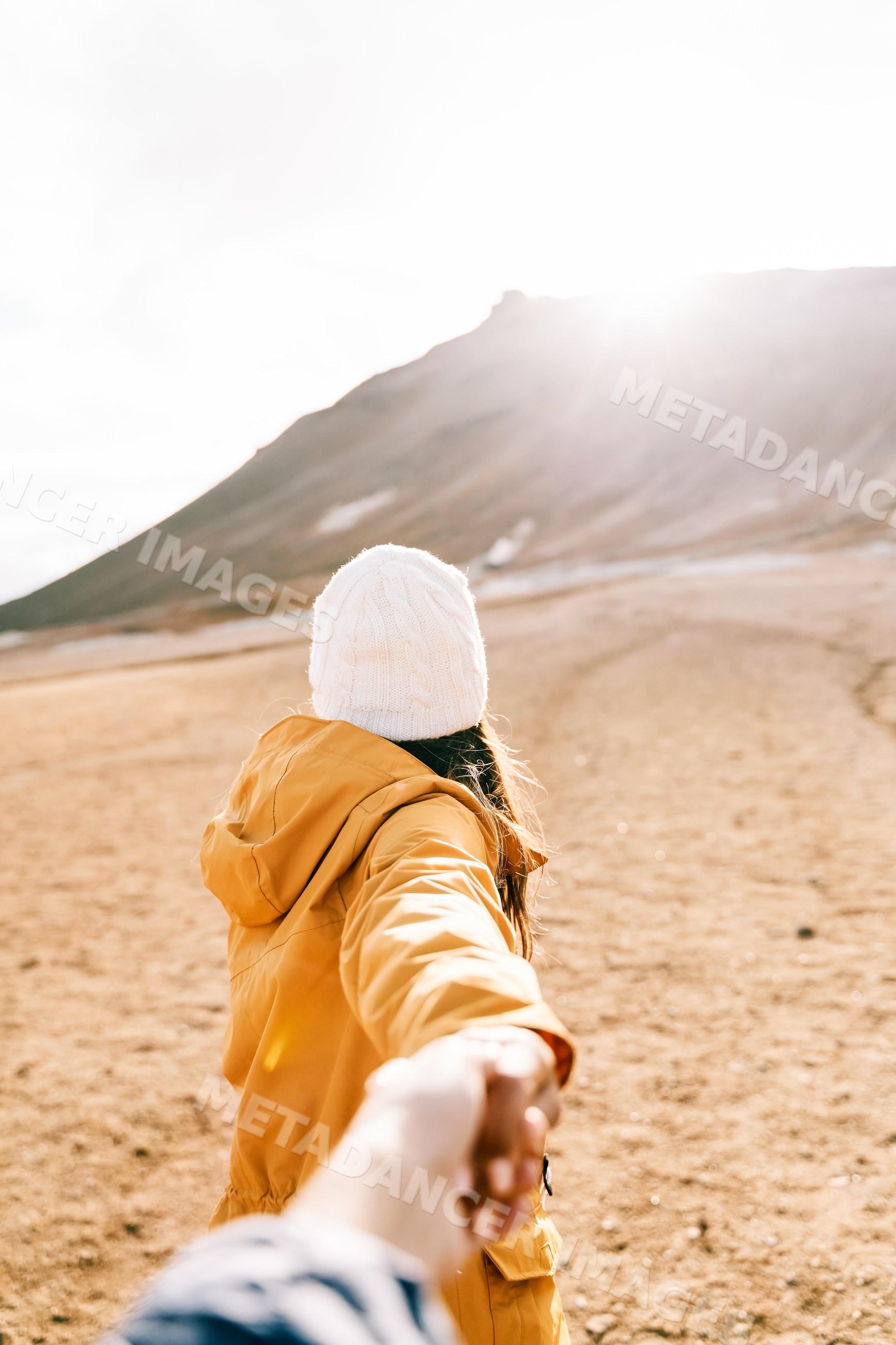A white woman holding a hand walks toward a mountain trail
