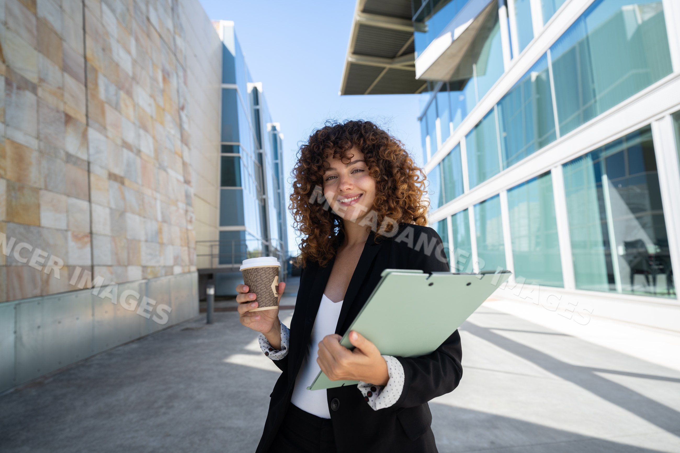 Businesswoman holding coffee and clipboard outside modern office