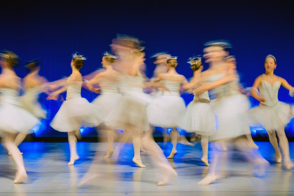 Female ballet dancers perform a group dance on stage in white tutus