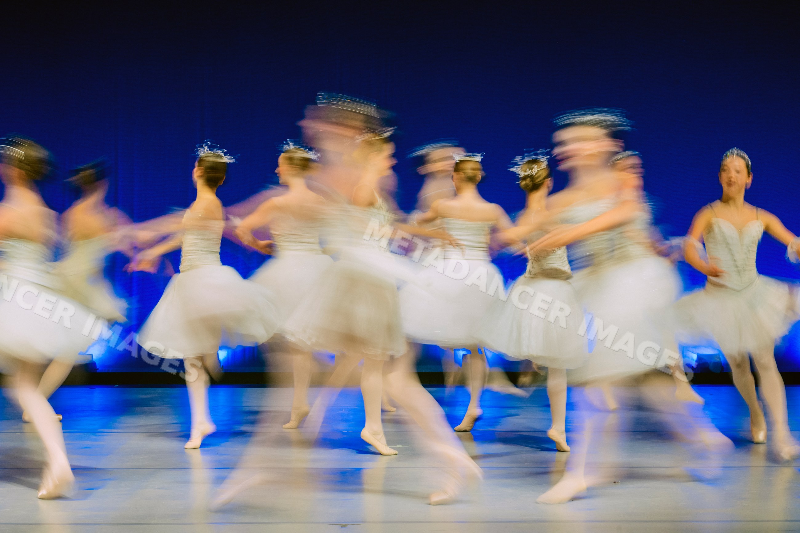 Female ballet dancers perform a group dance on stage in white tutus