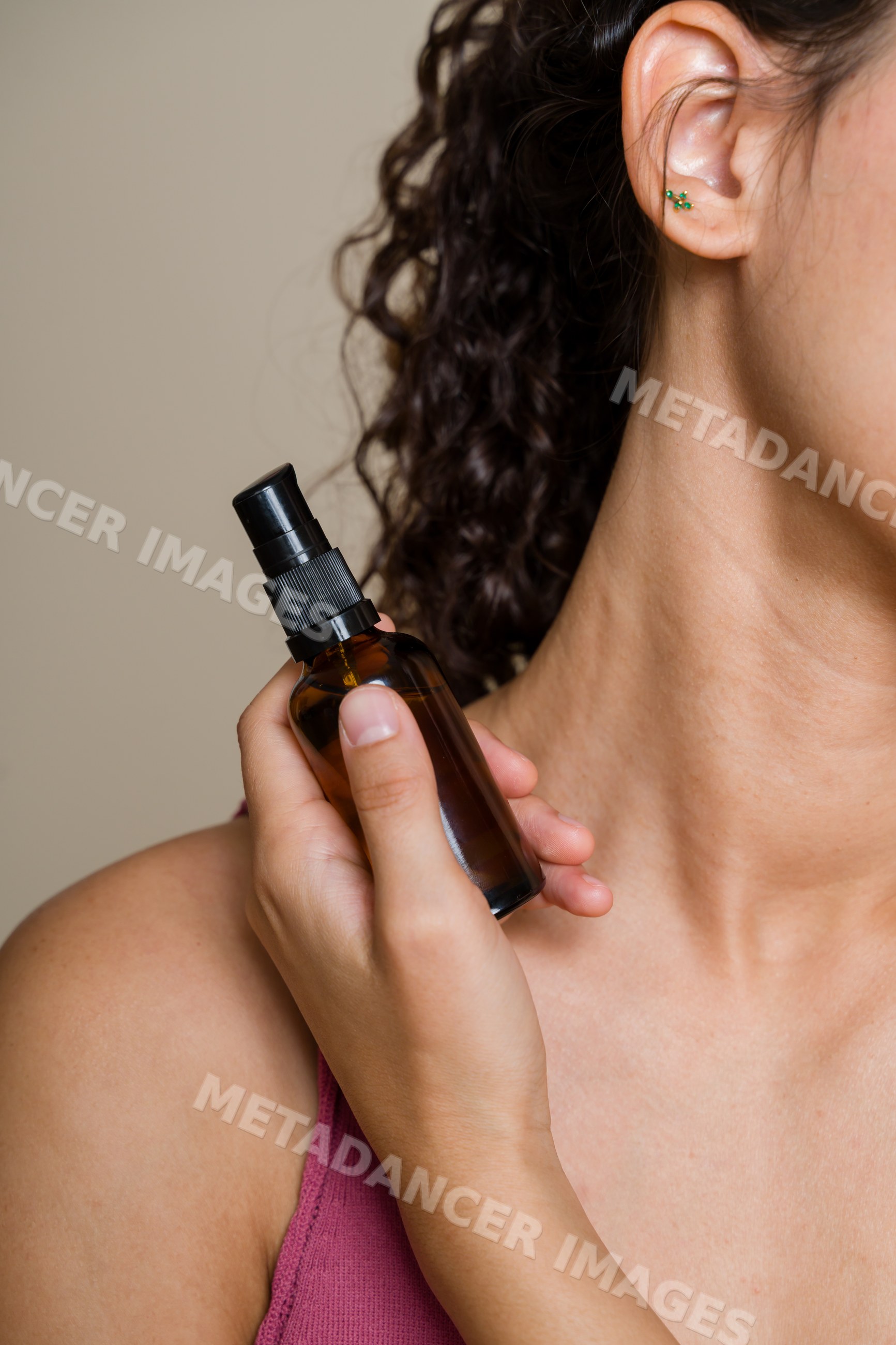 Hispanic woman holding amber spray bottle near neck in beauty shoot