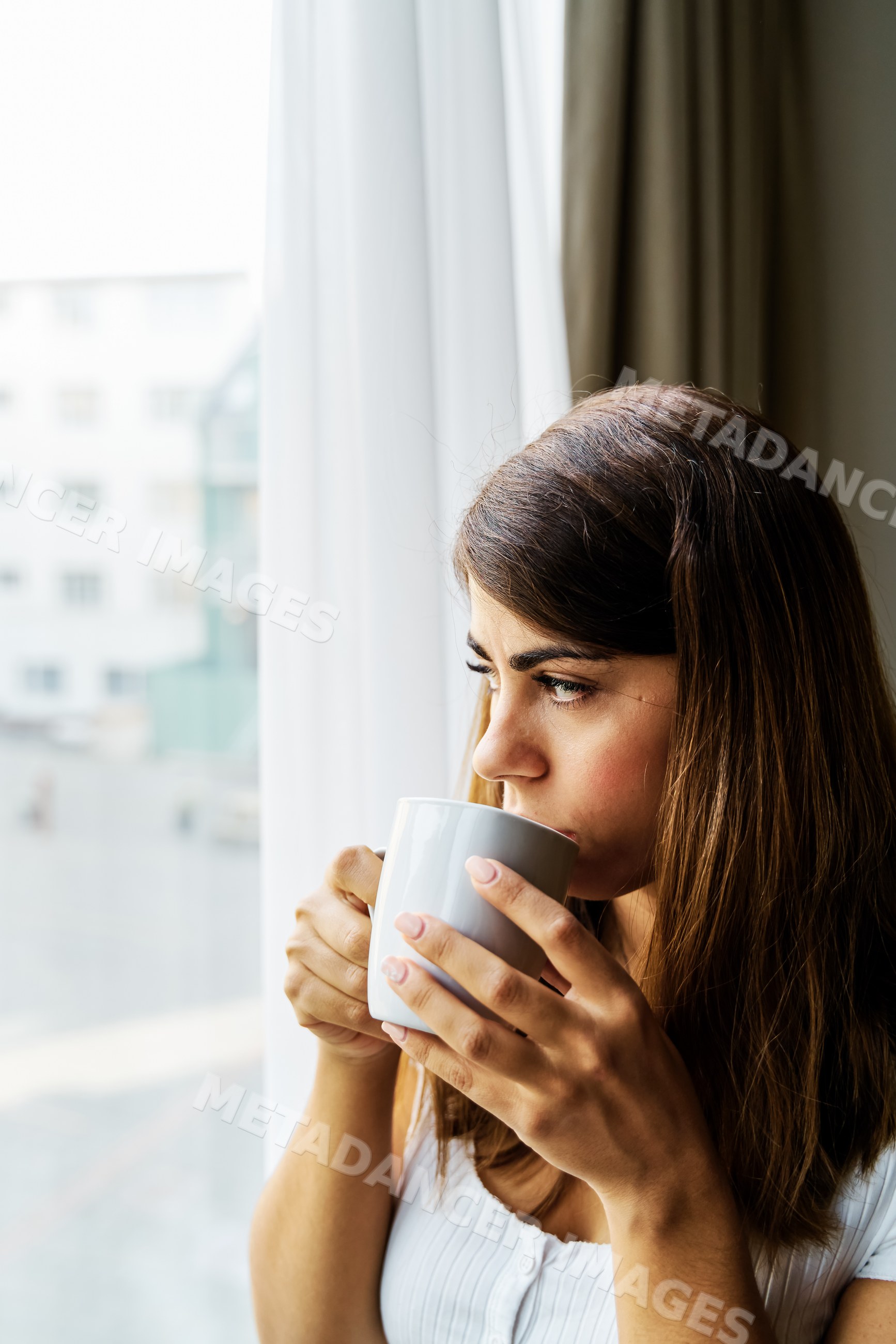 A woman drinks coffee looking out a window in an Iceland apartment