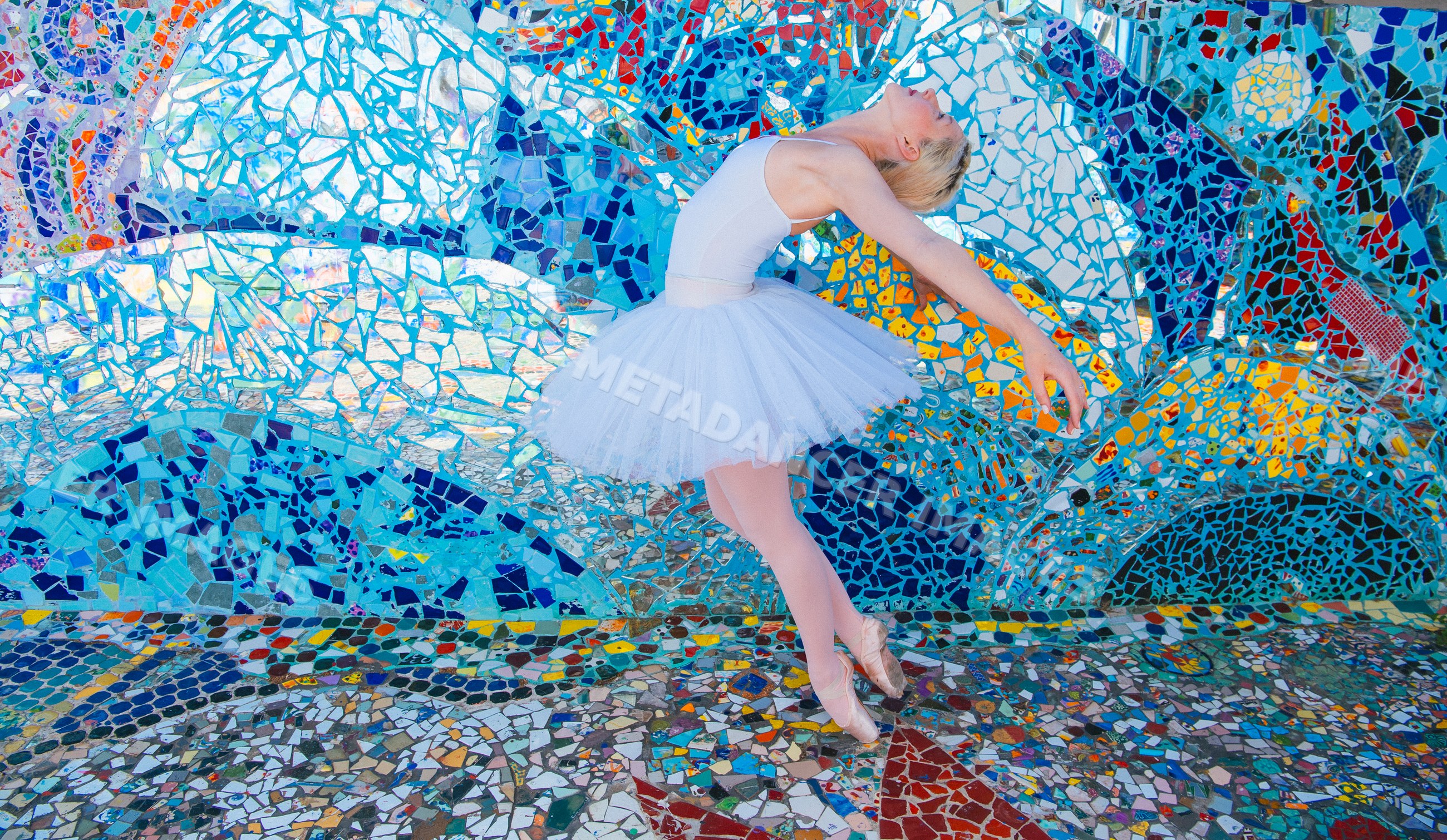 Ballet white dancer posing gracefully before colorful mosaic wall