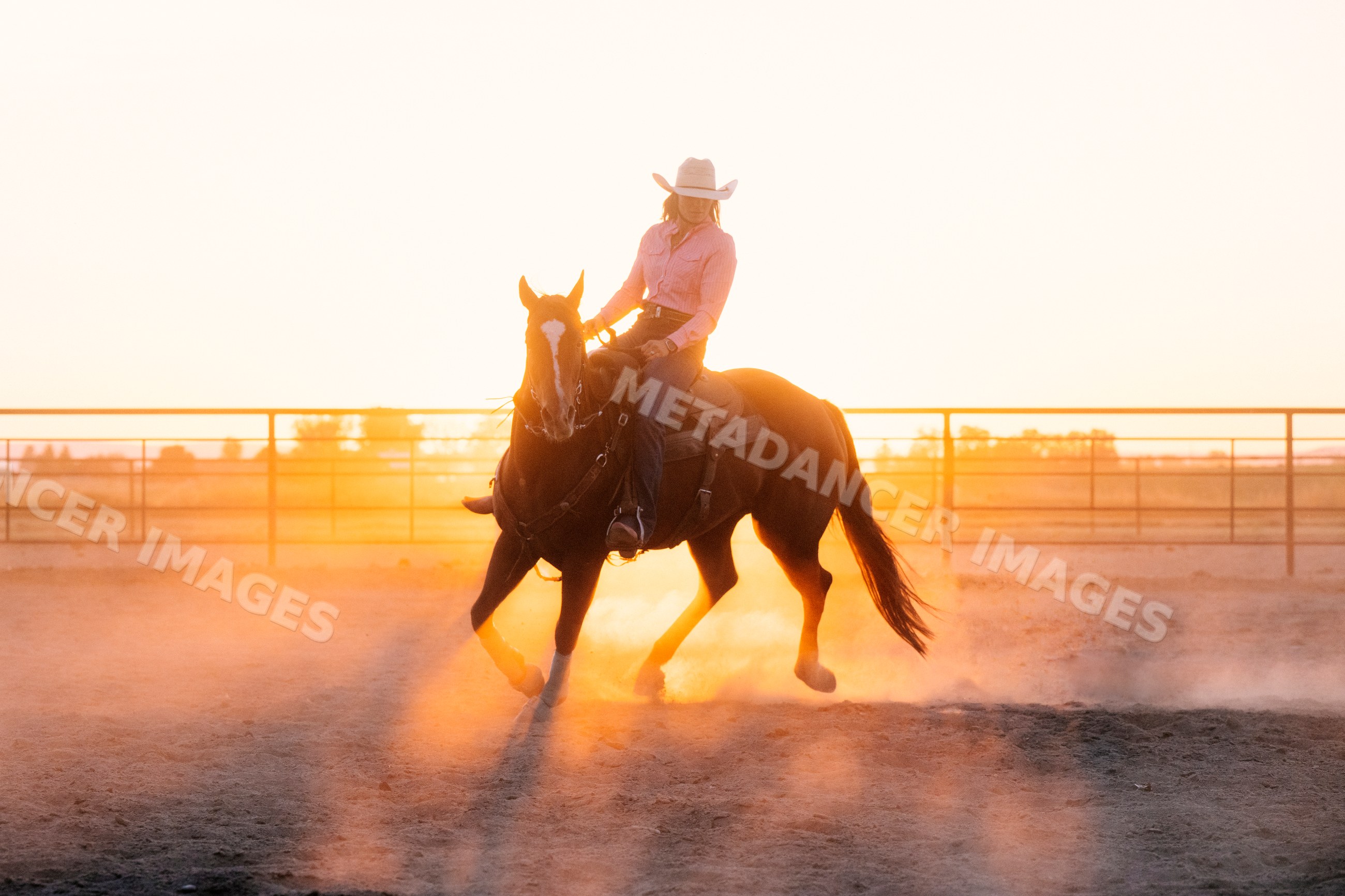 Cowgirl riding horse at dusty sunset in arena
