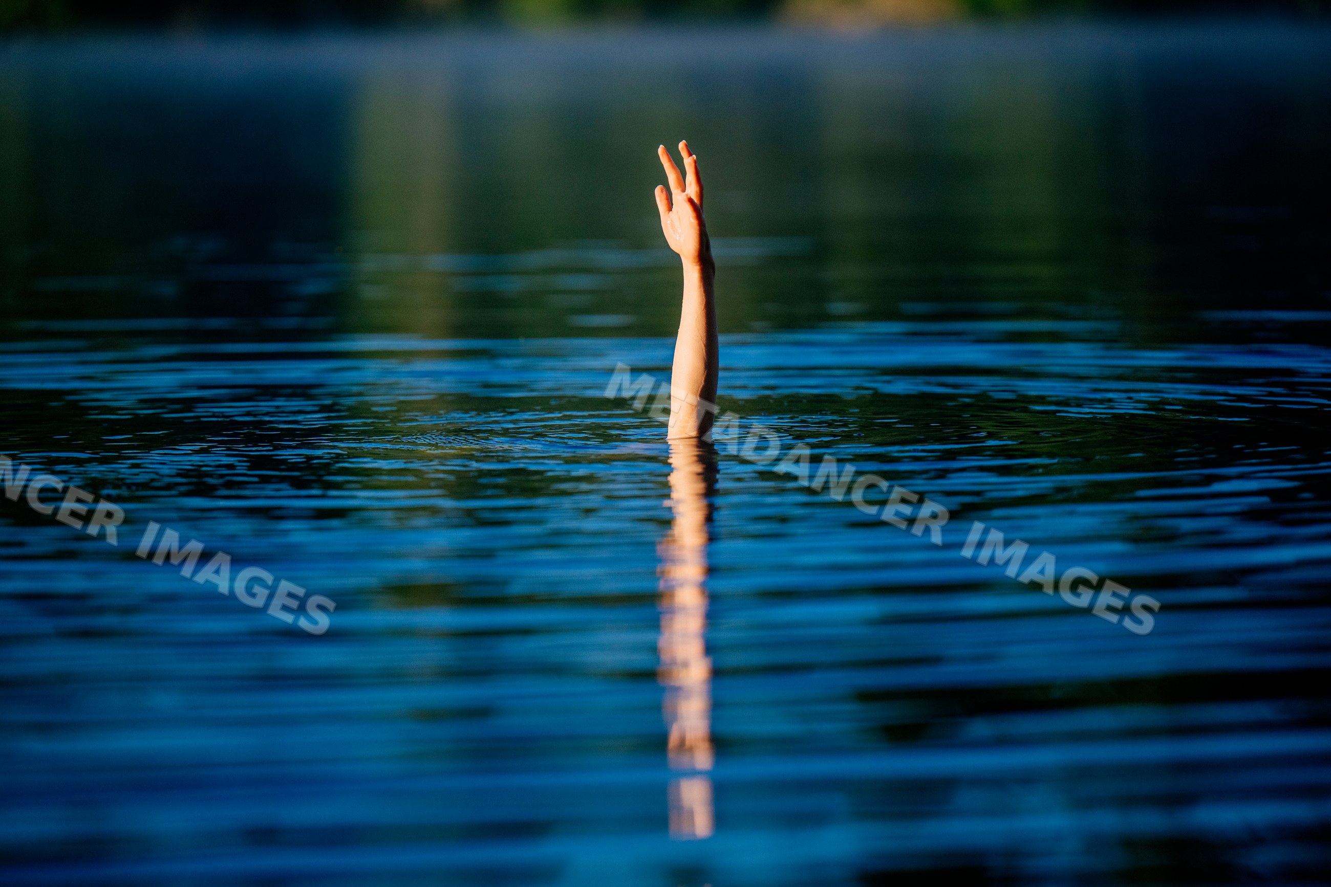 Hand raised above calm lake water surface