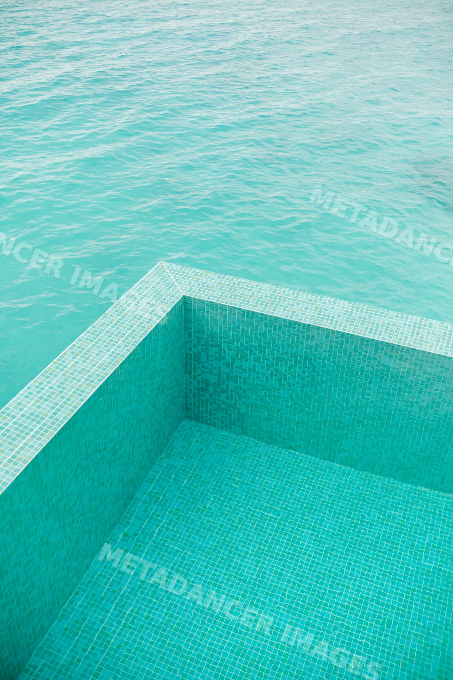 Turquoise tiled pool edge blending into calm sea water