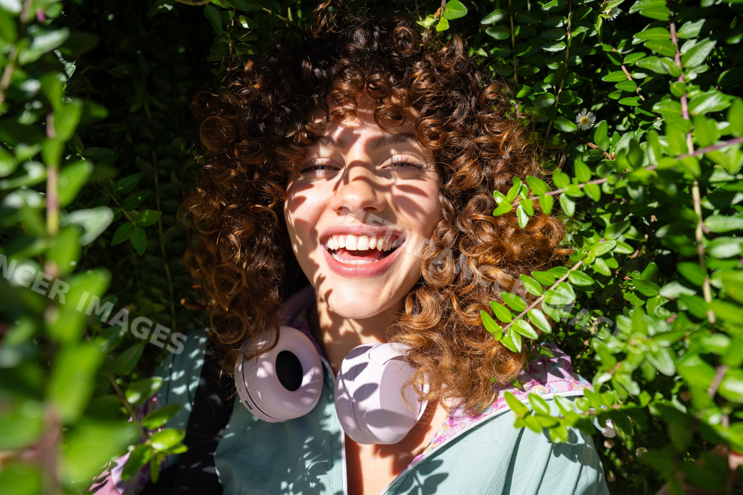 White woman smiling outdoors with headphones and curly hair