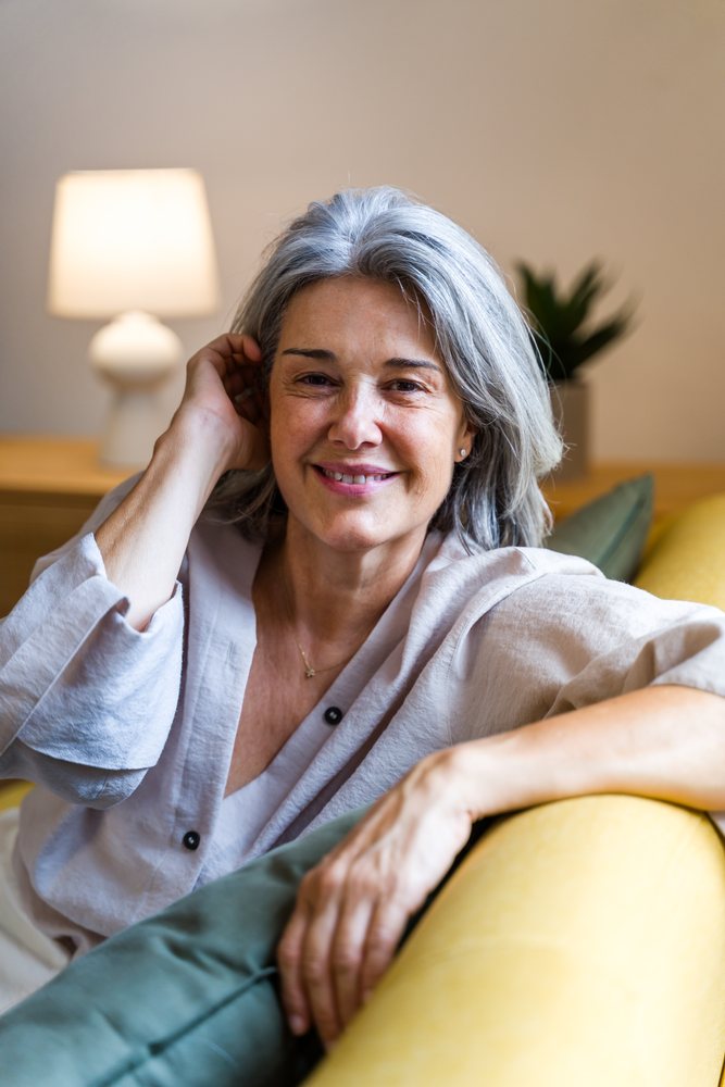 White woman with grey hair smiling and relaxing on couch indoors