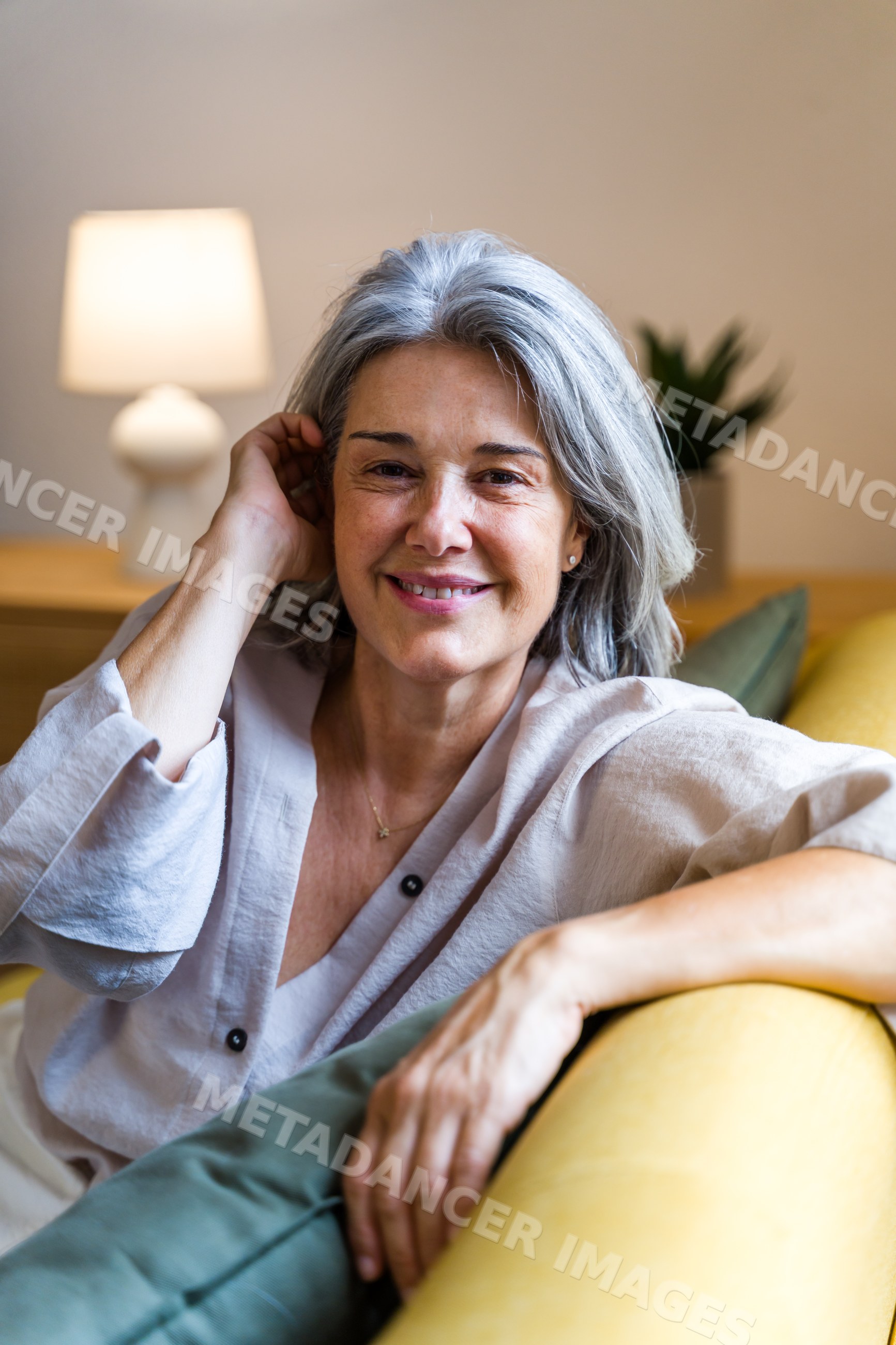 White woman with grey hair smiling and relaxing on couch indoors