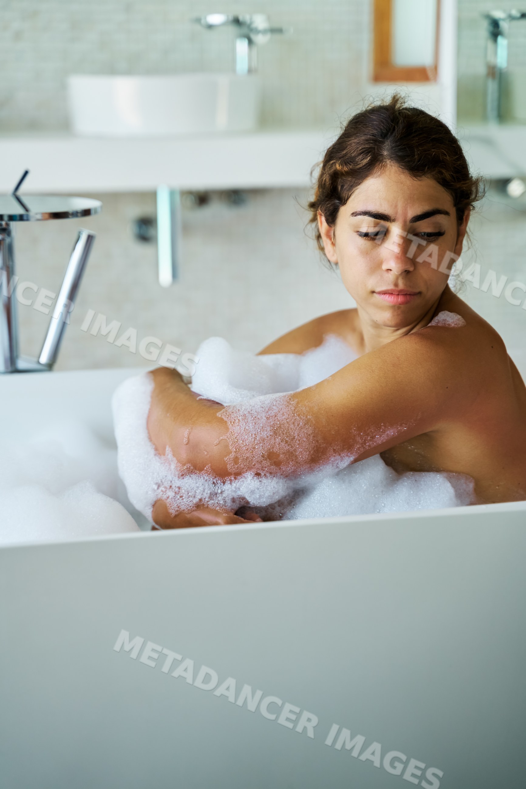 A white woman relaxing in a bubble bath in a modern bathroom