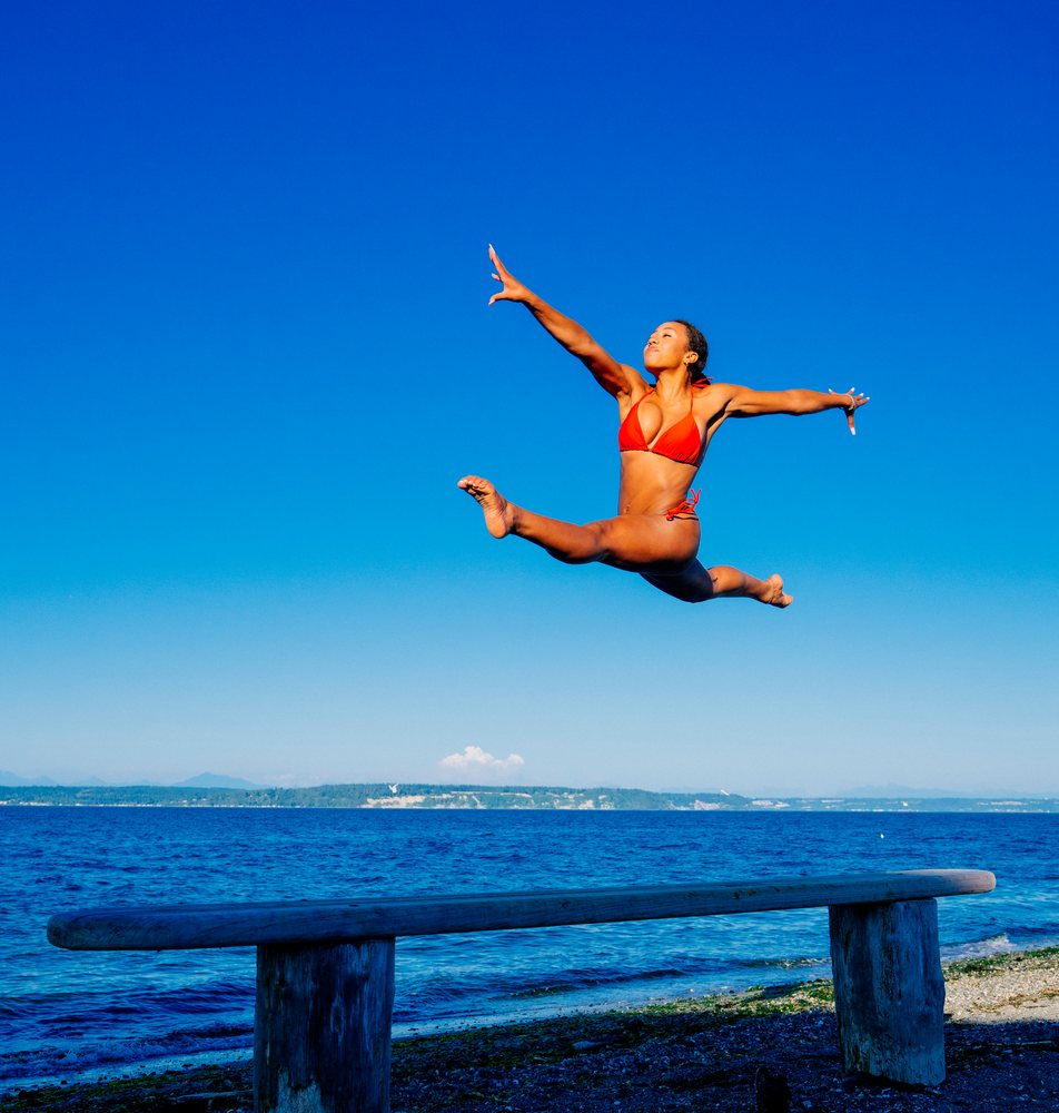 Woman jumping in split leap pose on beach in washington USA