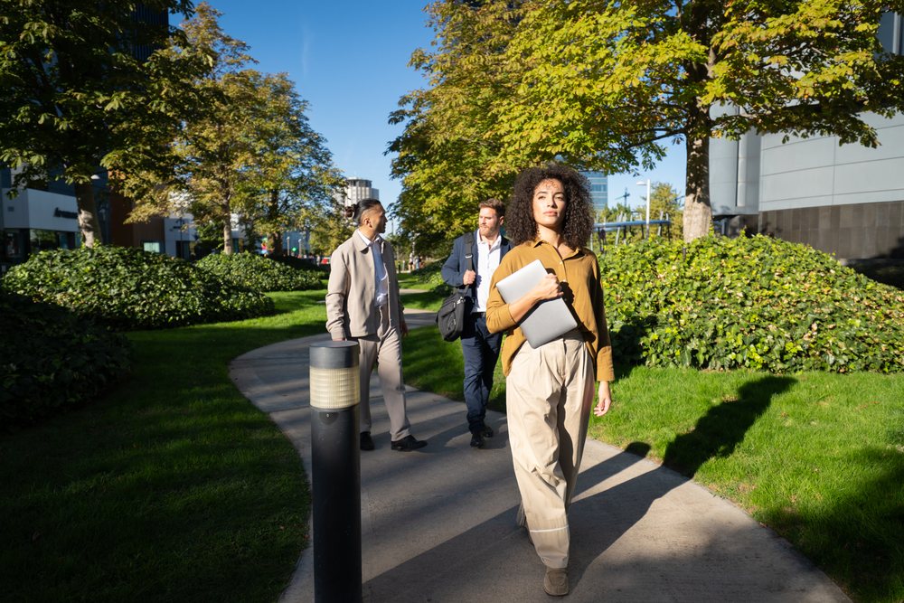White woman walking in urban park in Madrid holding laptop with men