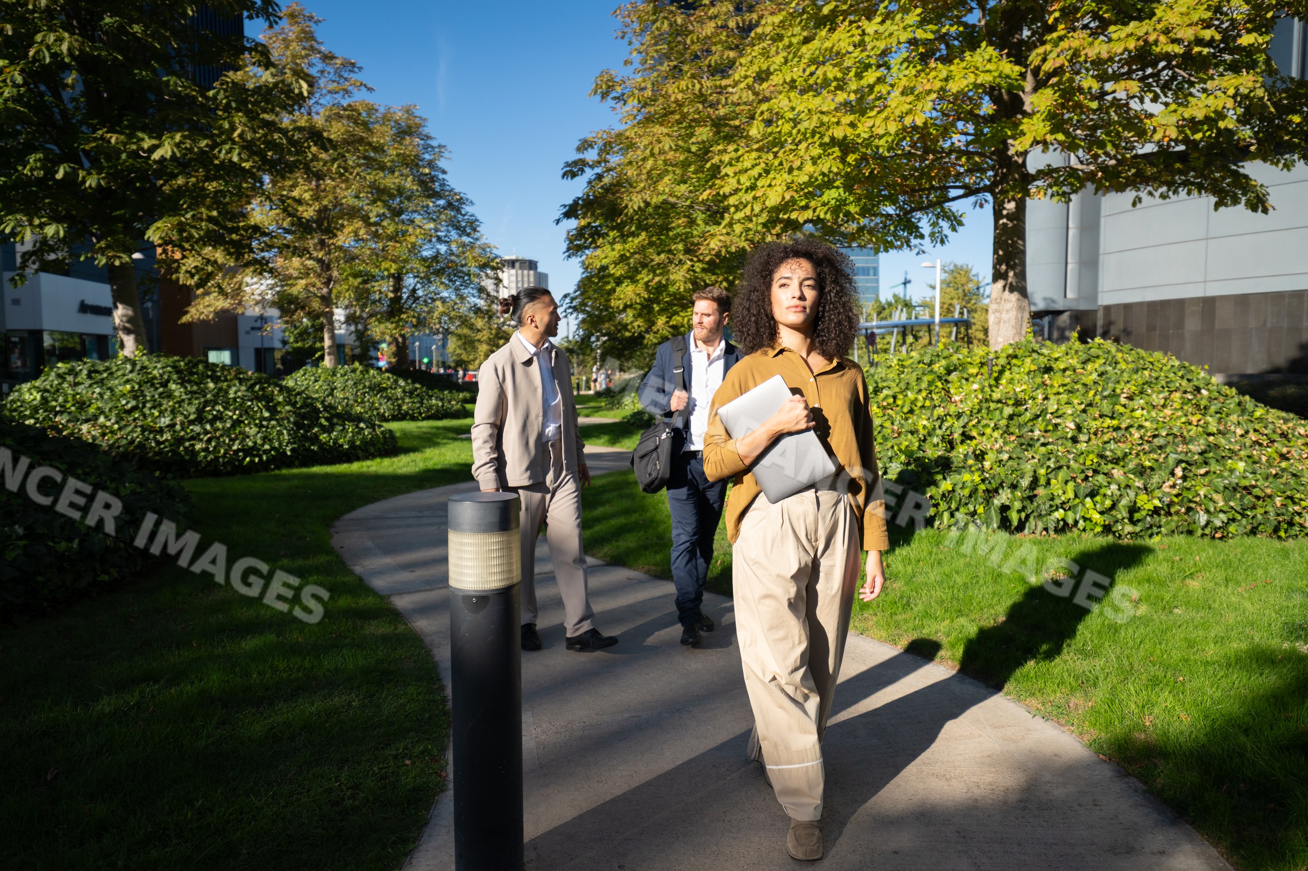 White woman walking in urban park in Madrid holding laptop with men