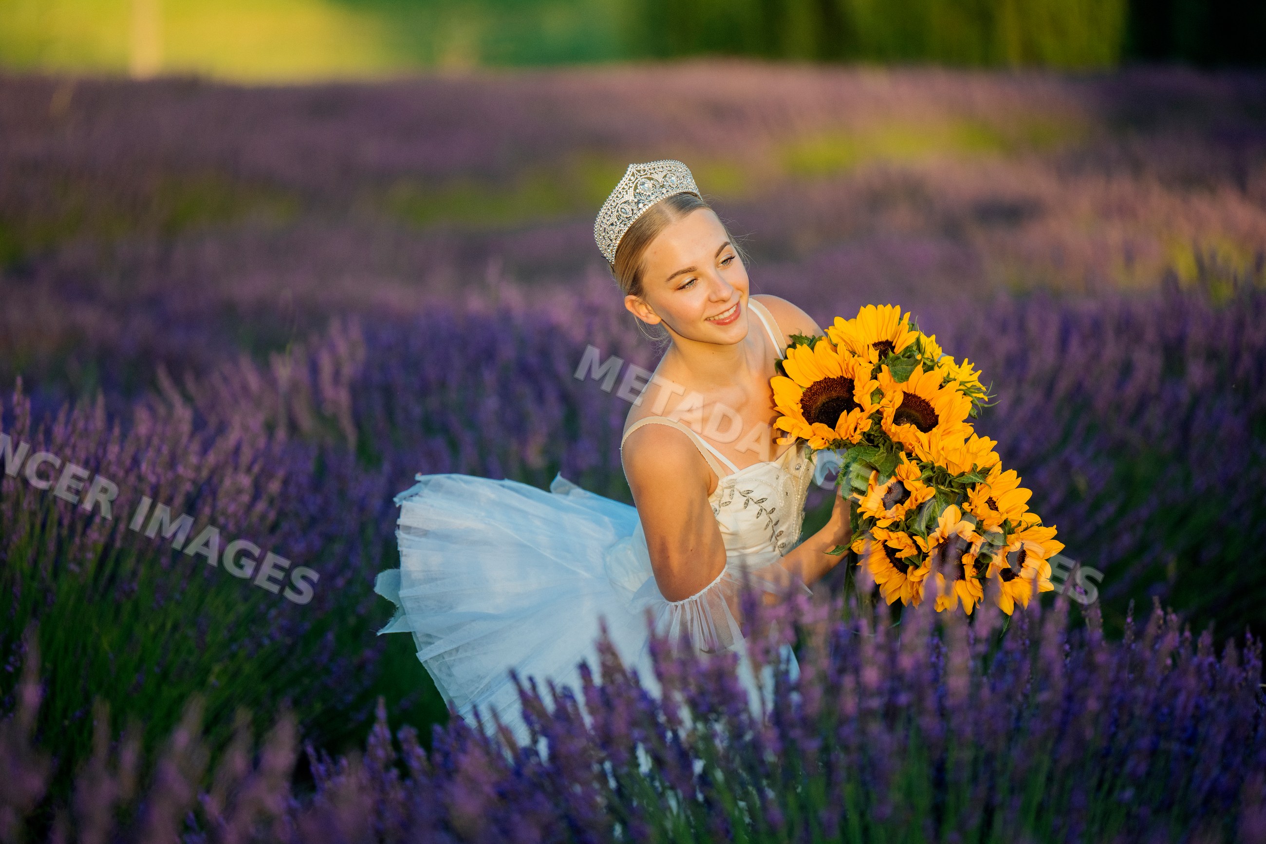 A ballet white dancer wearing a tiara holds sunflowers