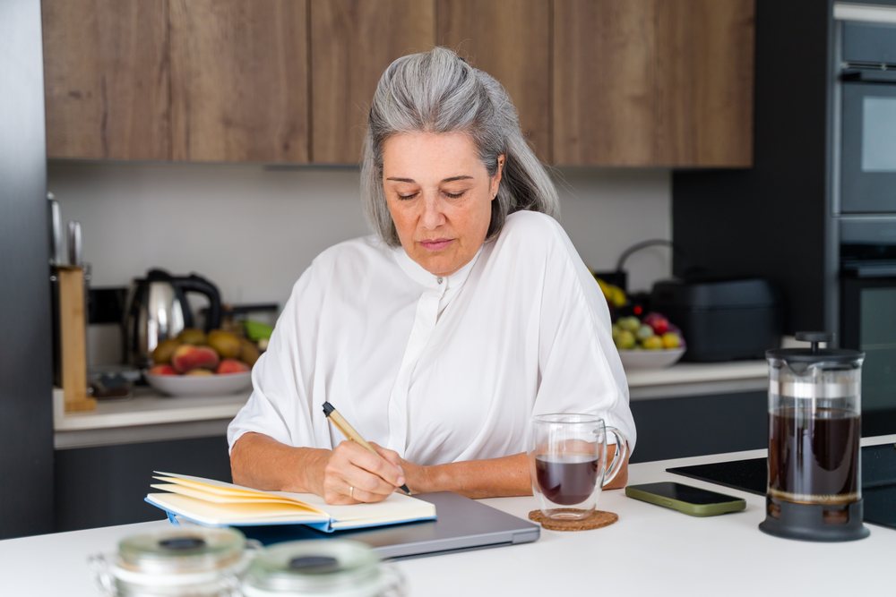 White Woman writing notes in a modern kitchen with coffee in a kitchen