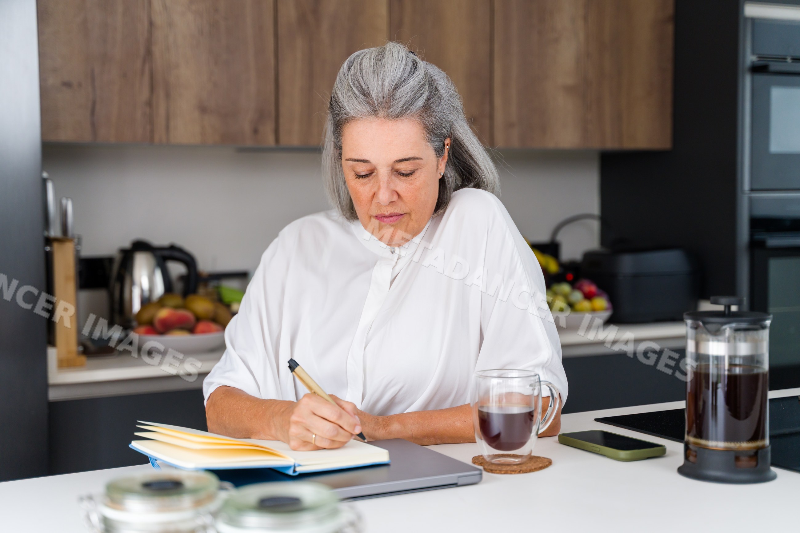 White Woman writing notes in a modern kitchen with coffee in a kitchen