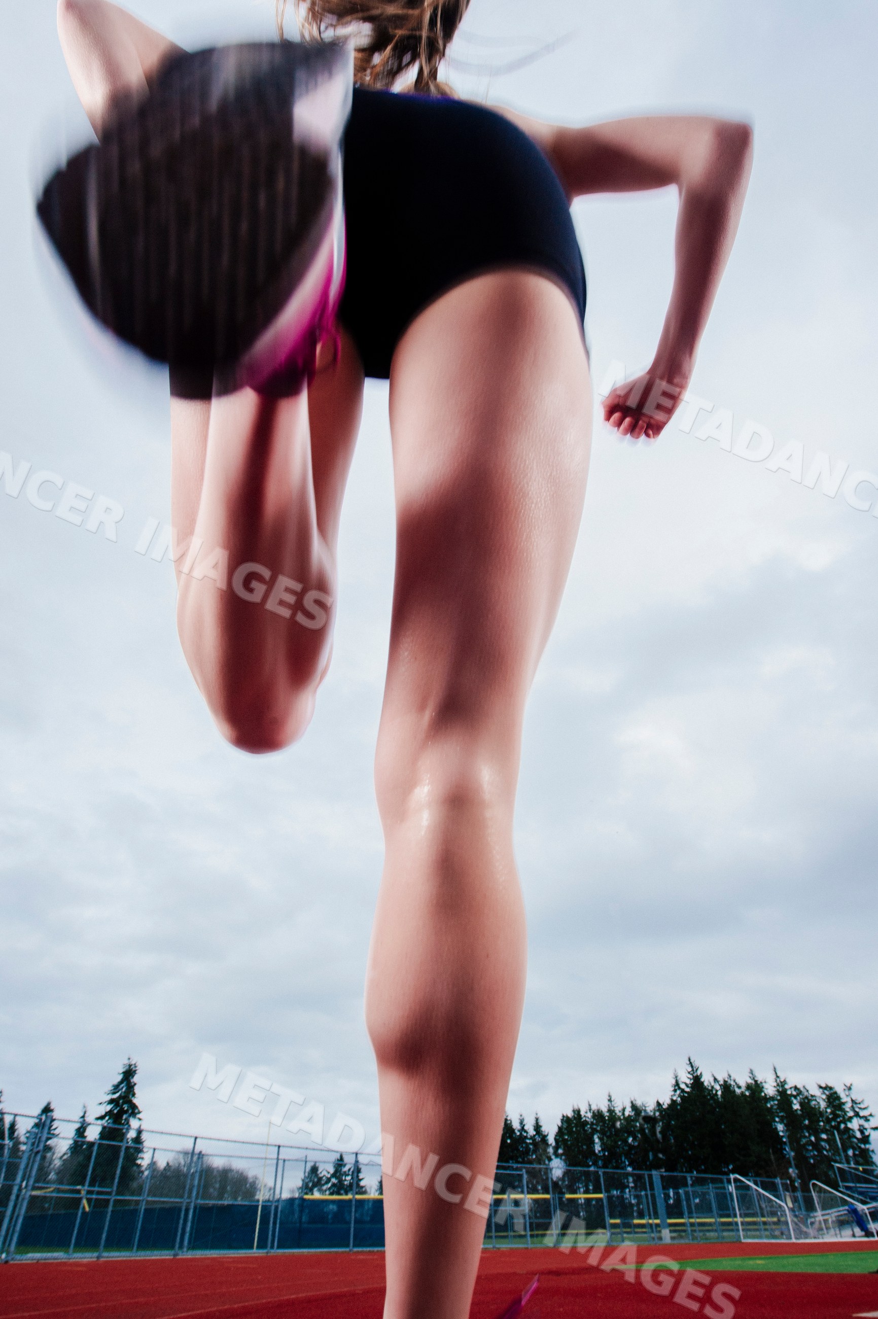 White athlete sprinting on track outdoors with stadium and trees