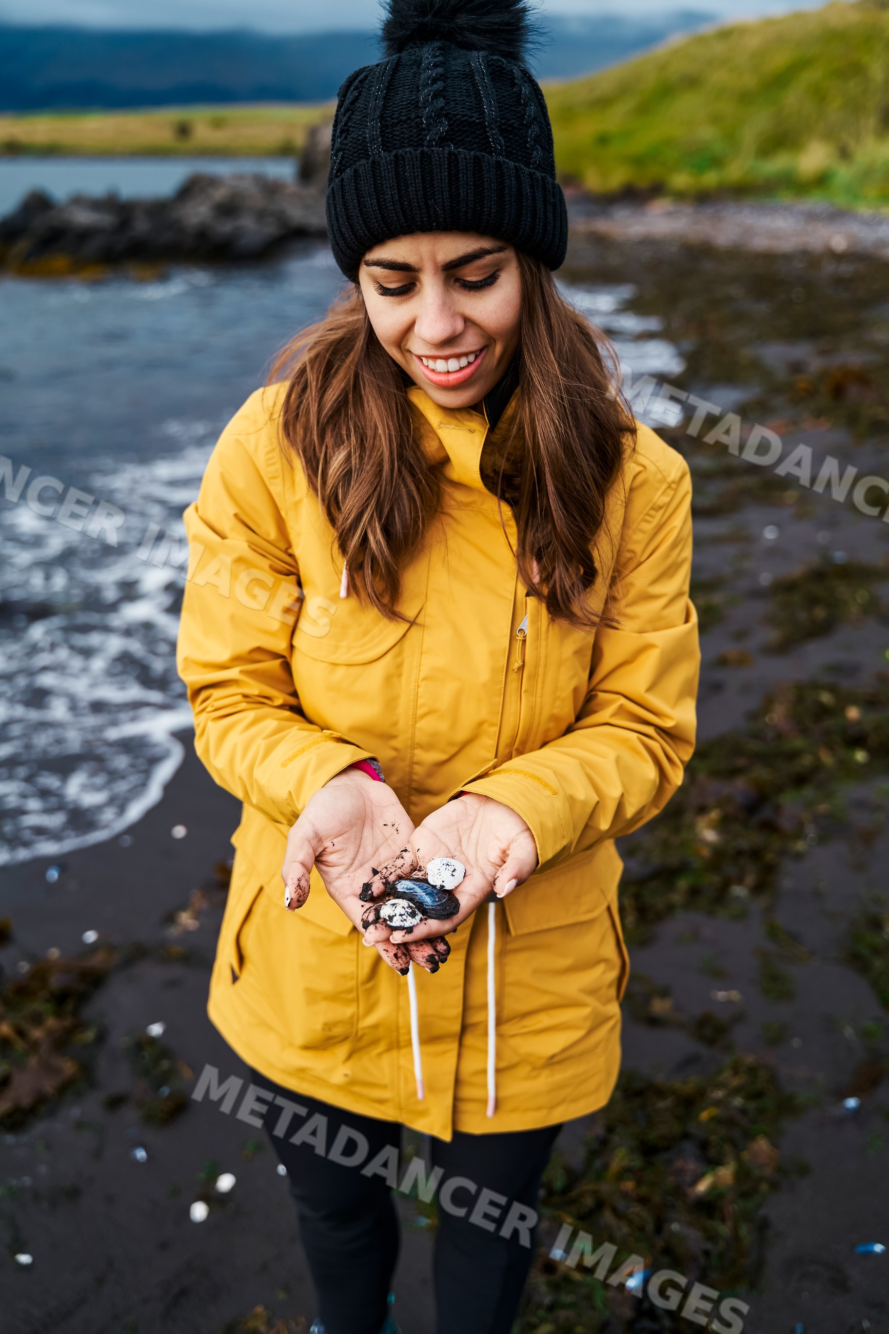 White Woman holding seashells on a black sand beach in a beach