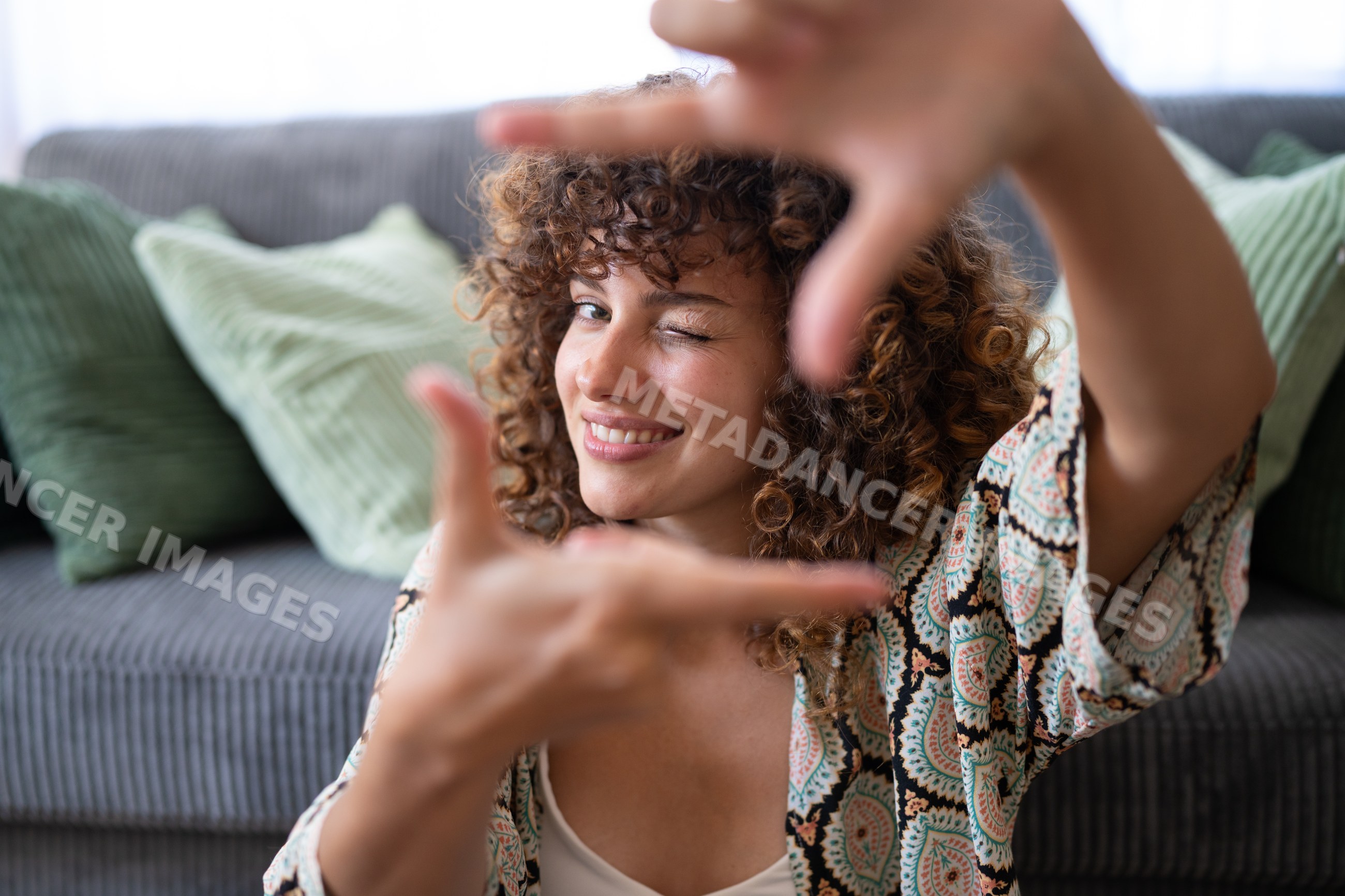 White woman with curly hair winking and framing face indoors
