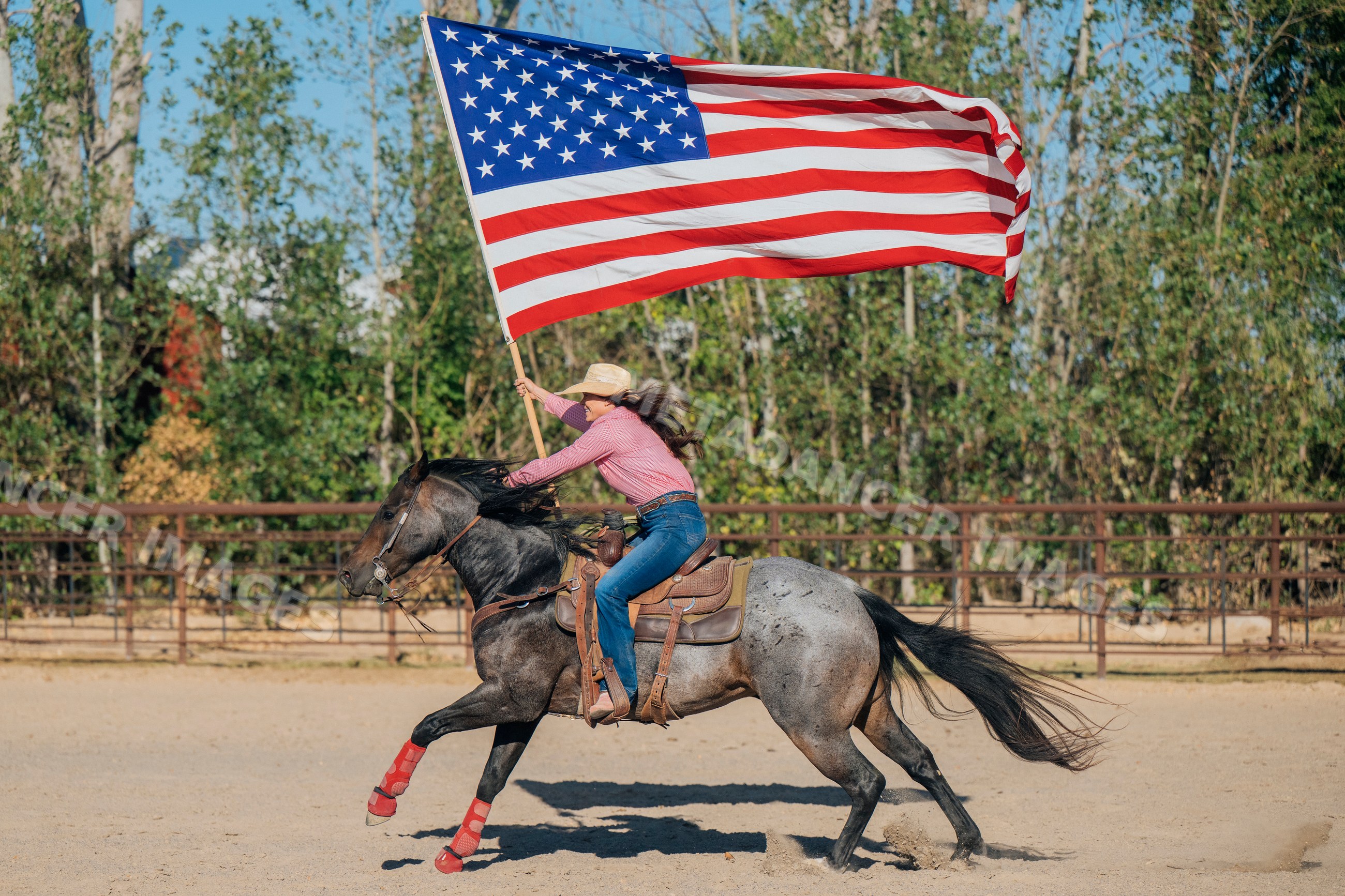 White woman riding horse holding american flag in outdoor arena