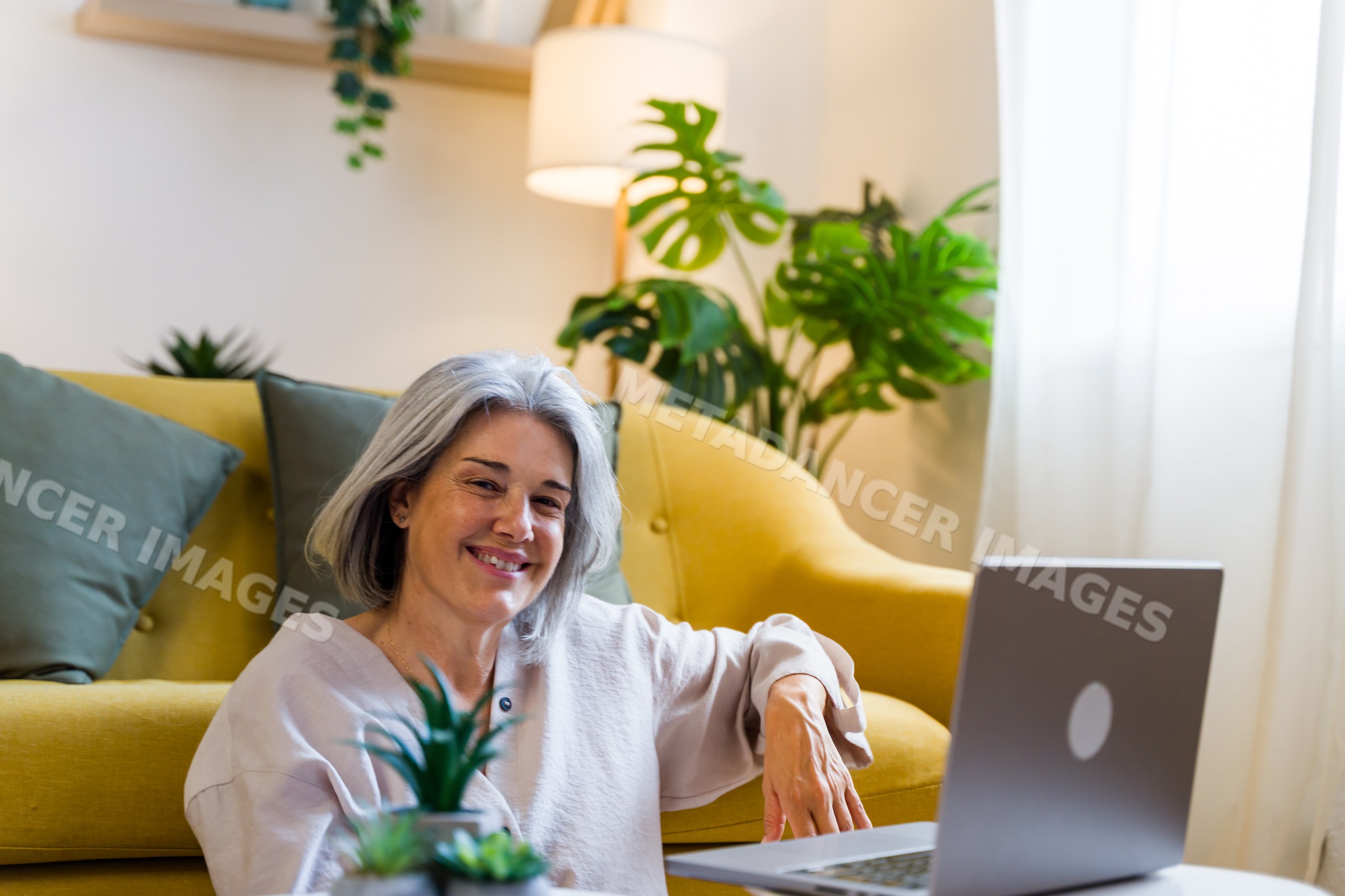 White woman using laptop in cozy living room with yellow sofa