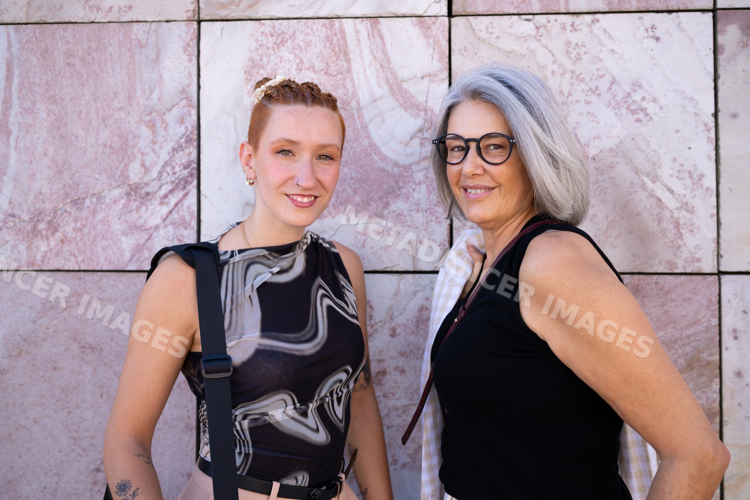 Two white women smiling and posing outdoors against a pink marble wall