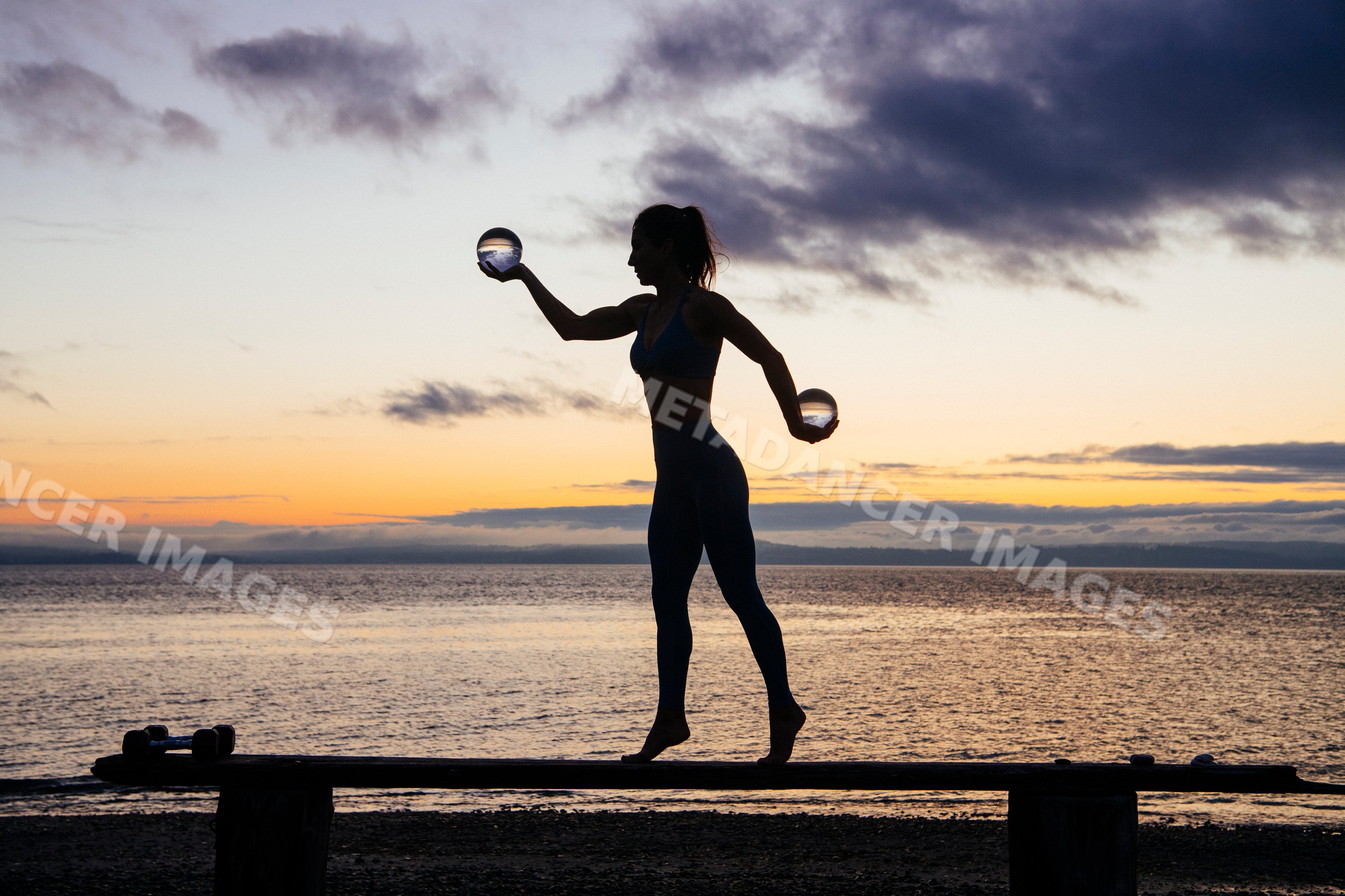 Silhouette of white woman balancing with crystal balls at ocean sunset