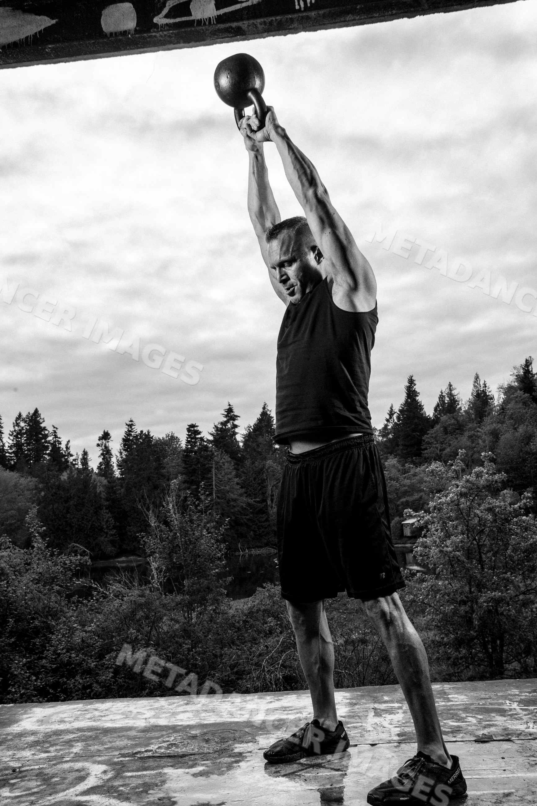 White man lifting kettlebell overhead during outdoor workout