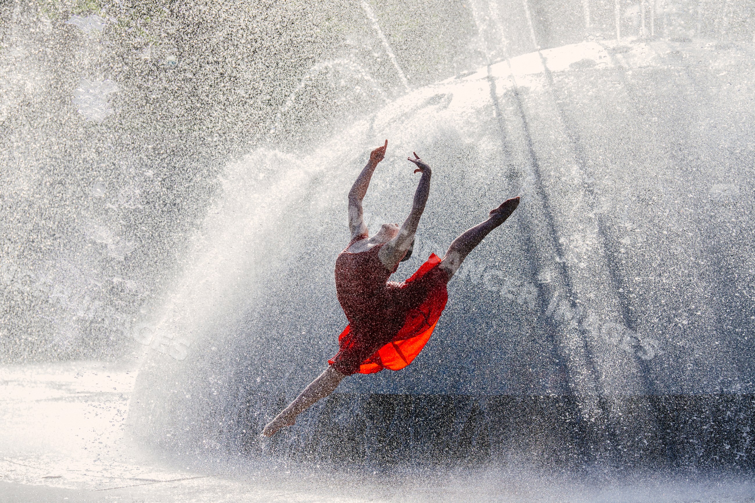 White dancer leaping in red dress through fountain water spray