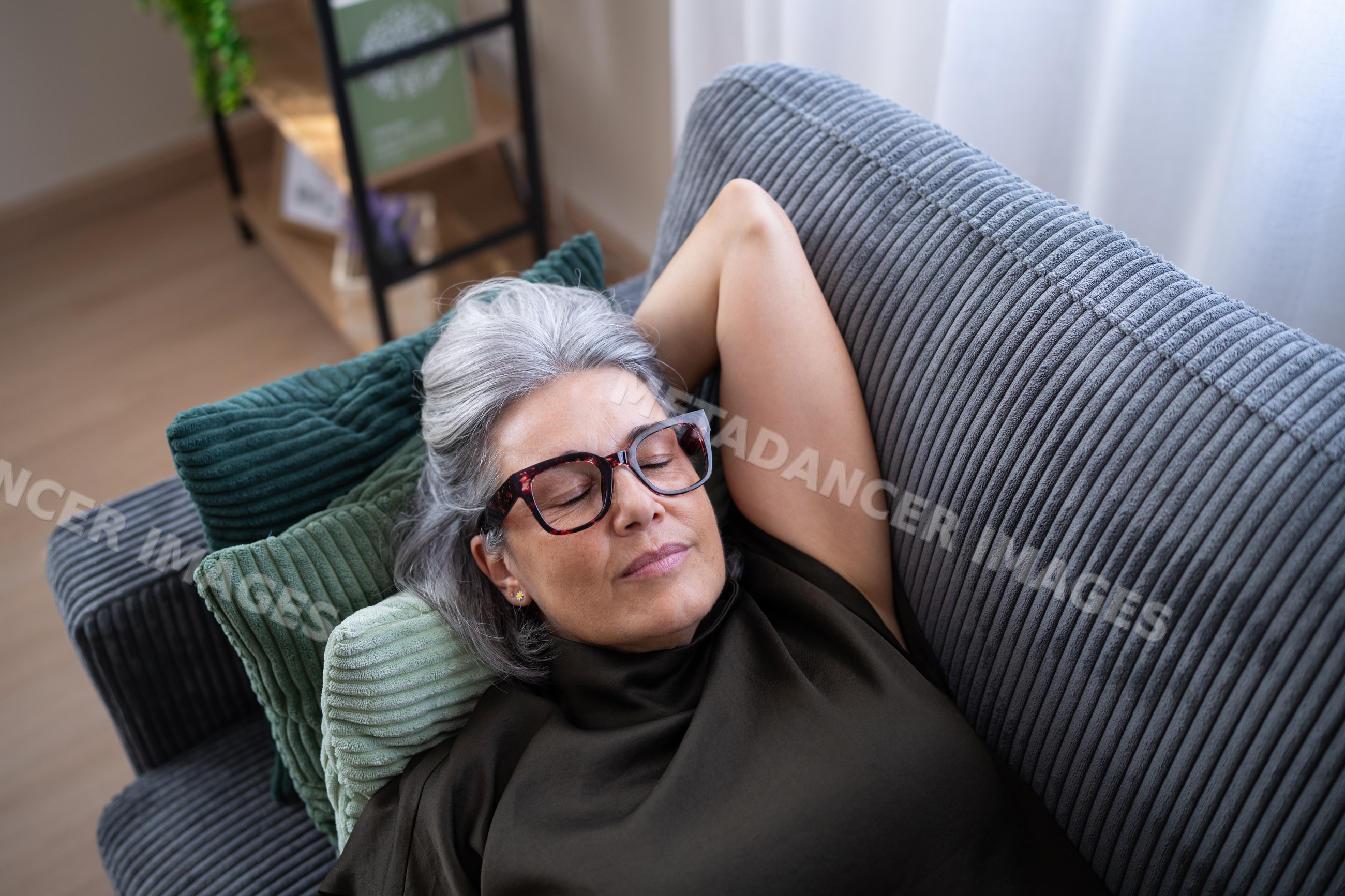White woman resting peacefully on a sofa with green cushions indoors