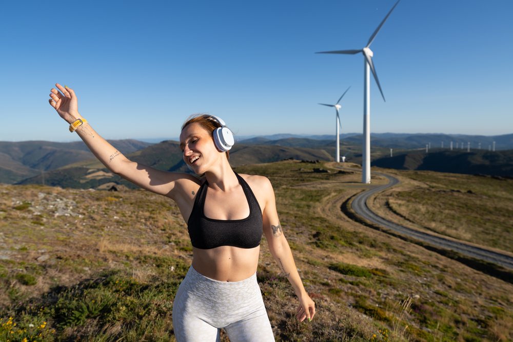 Young white woman dances happily near wind turbines in Galicia, Spain