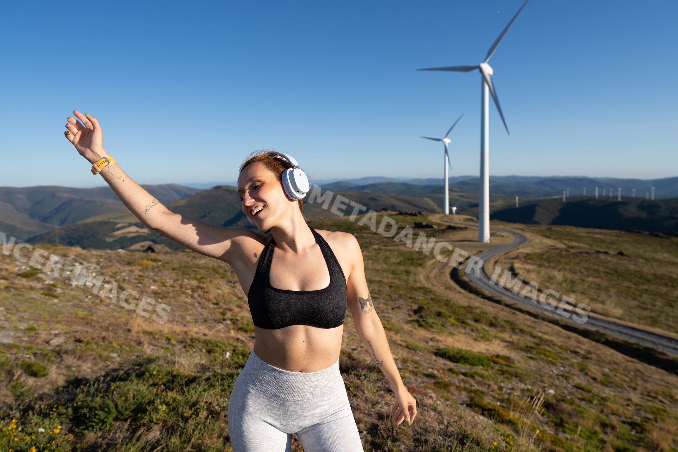 Young white woman dances happily near wind turbines in Galicia, Spain