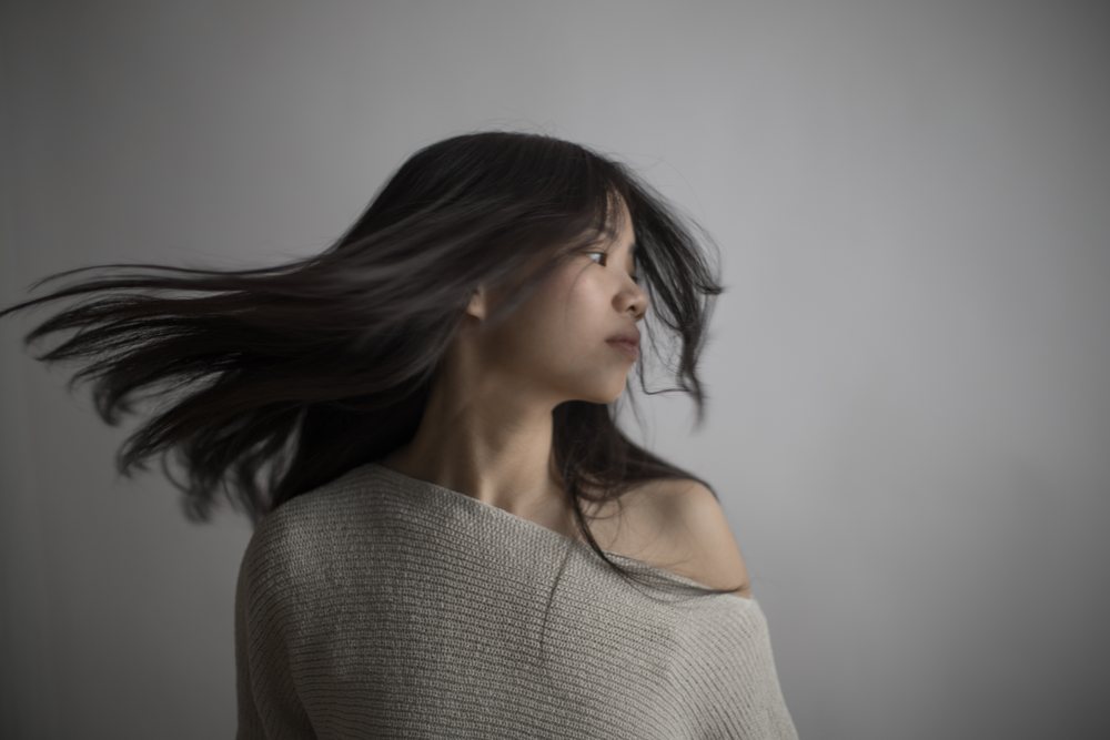 Southeast Asian woman turning head with flowing hair against gray