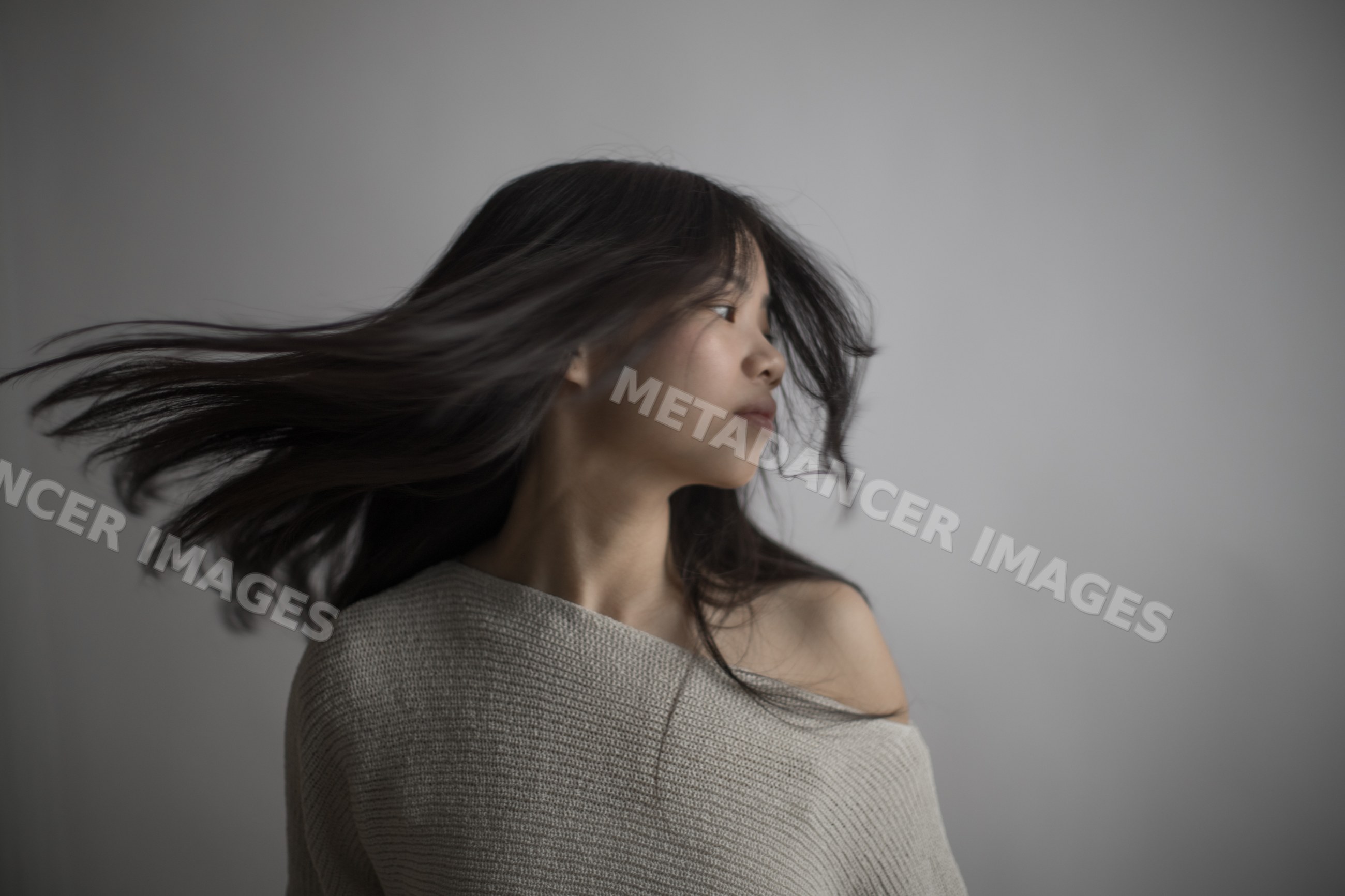 Southeast Asian woman turning head with flowing hair against gray