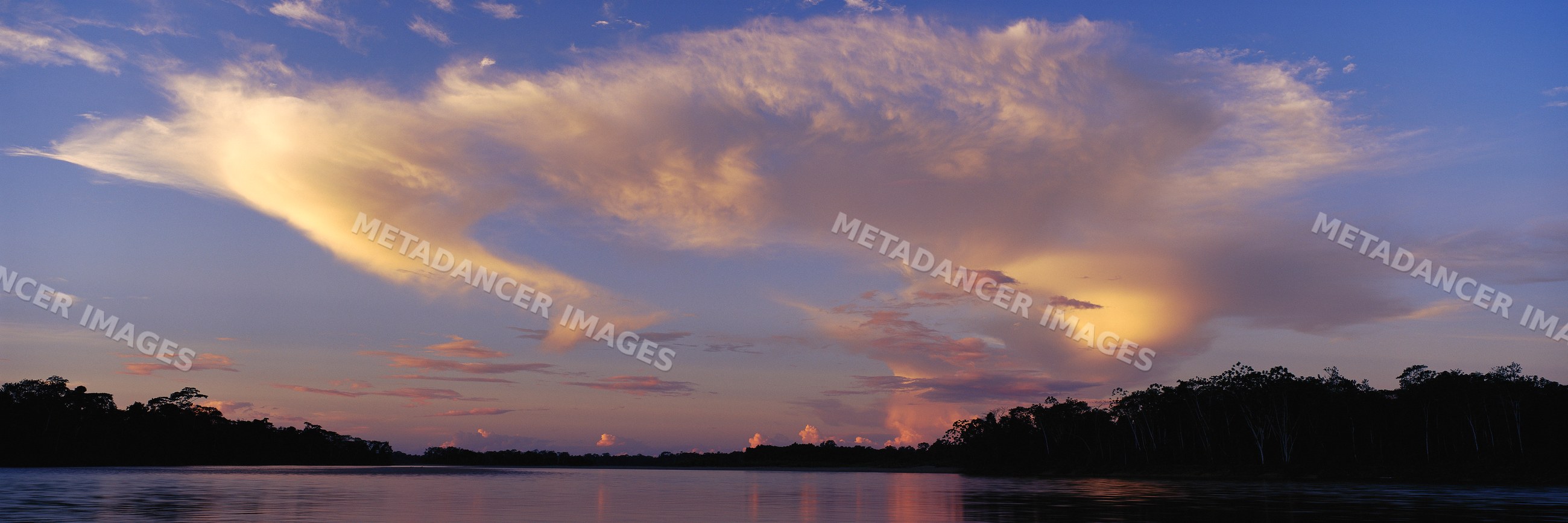 Sunset over river with silhouetted forest and vibrant clouds