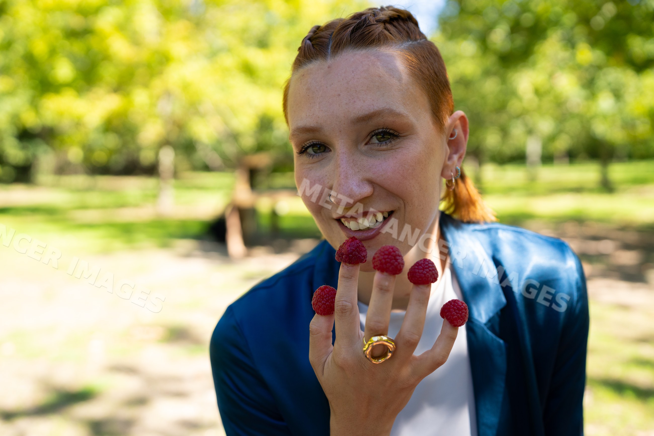 White woman smiling outdoors with raspberries on her fingers in a park