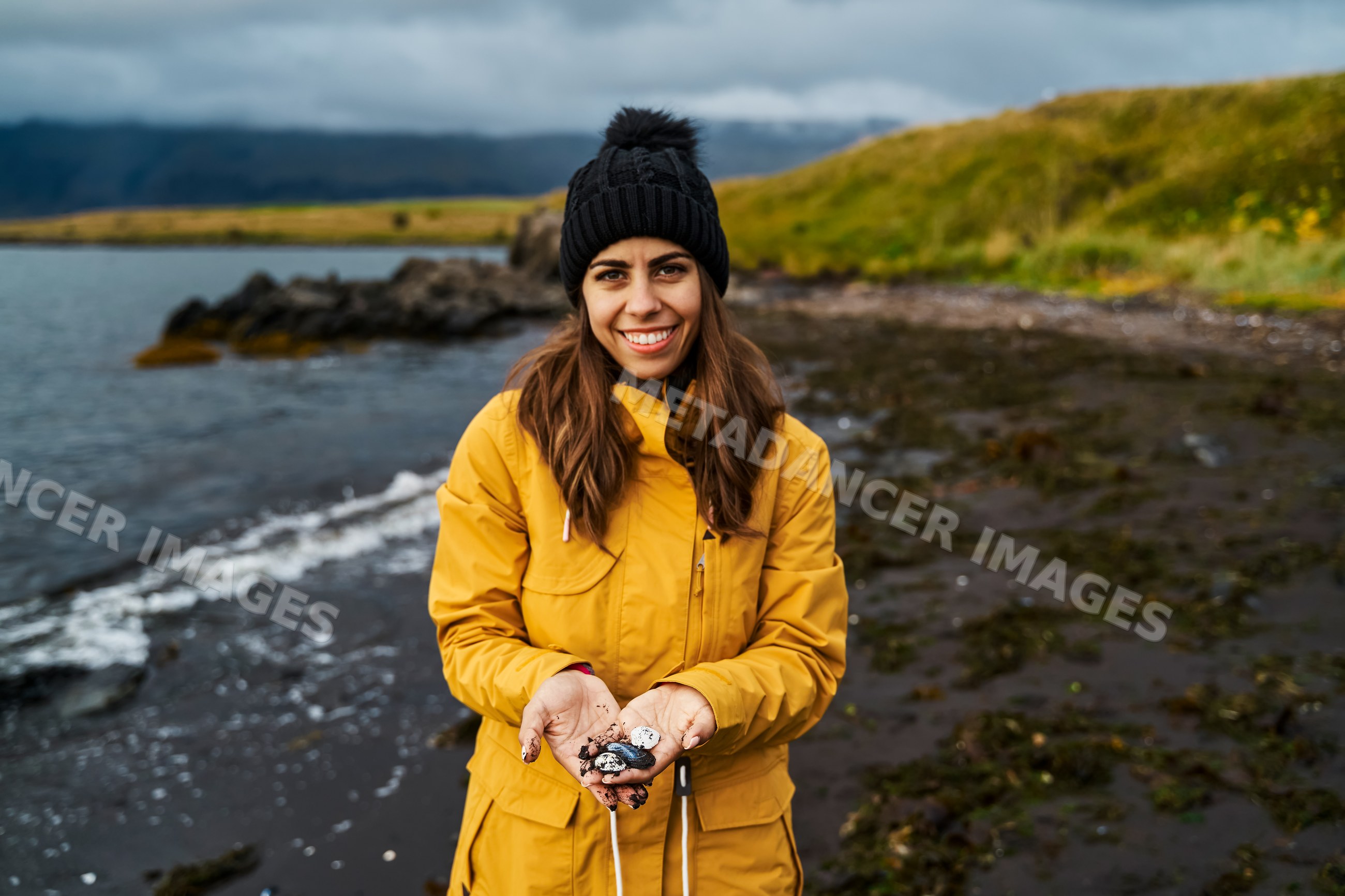 A white woman holding rocks on a black sand beach in a beach