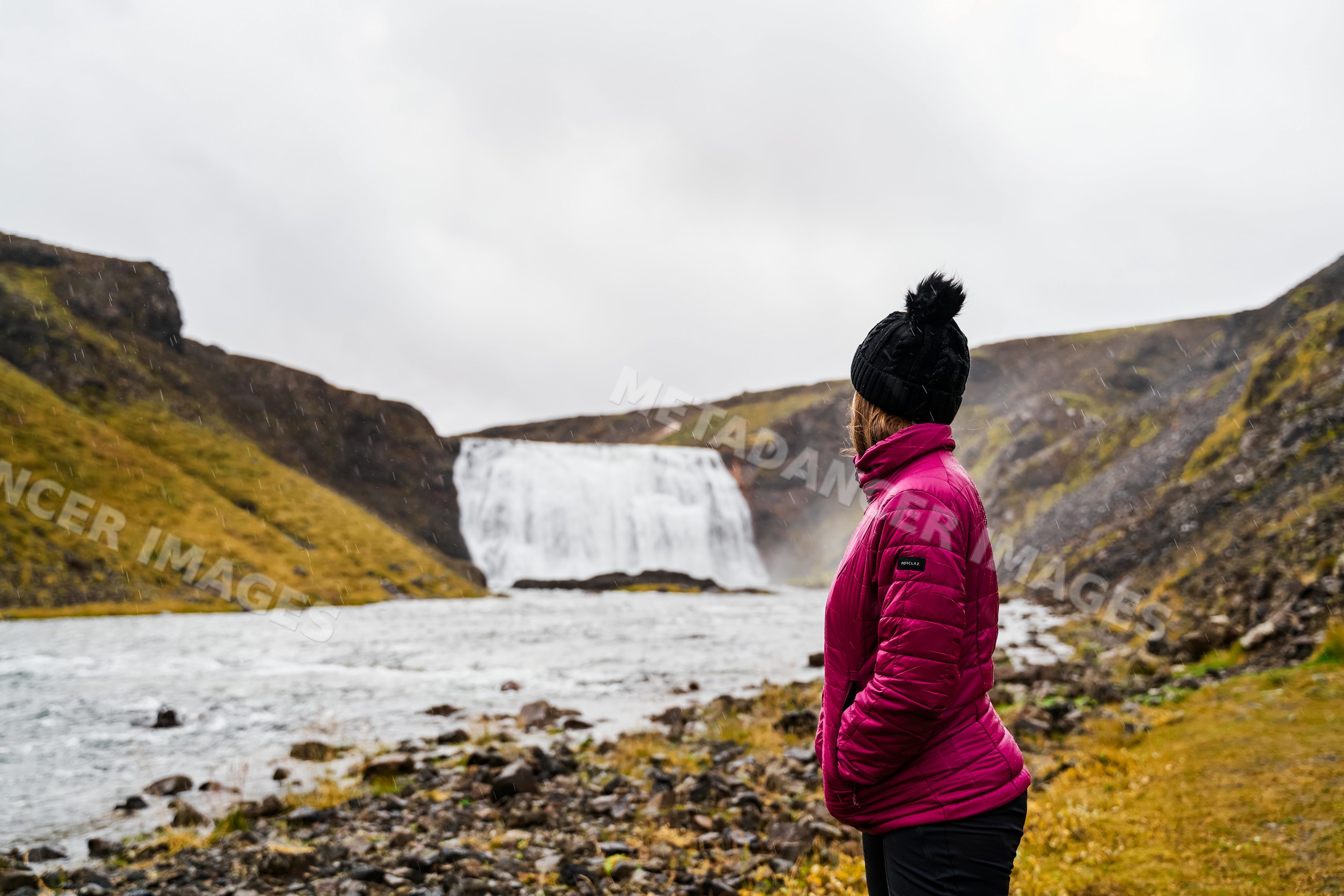 A white woman looking at a waterfall in a rocky mountain valley