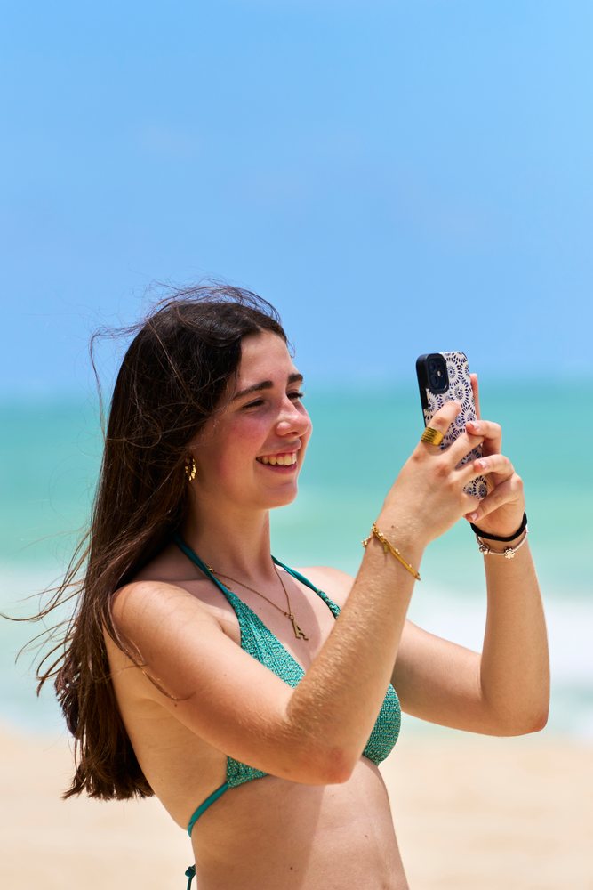 White woman taking photo with smartphone on beach in Hawaii, USA