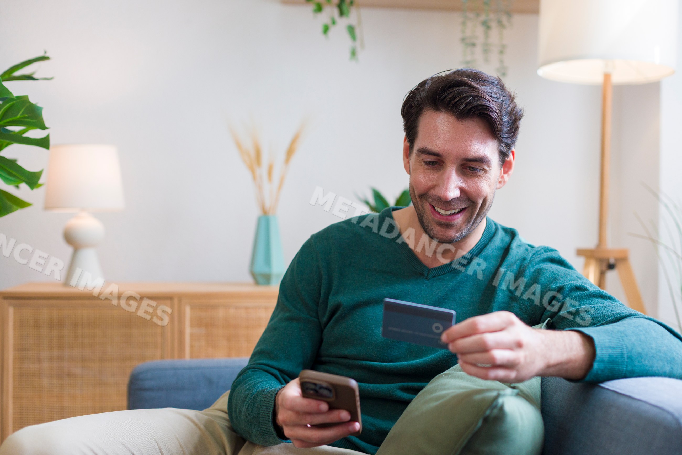 White man holding credit card using smartphone in modern living room