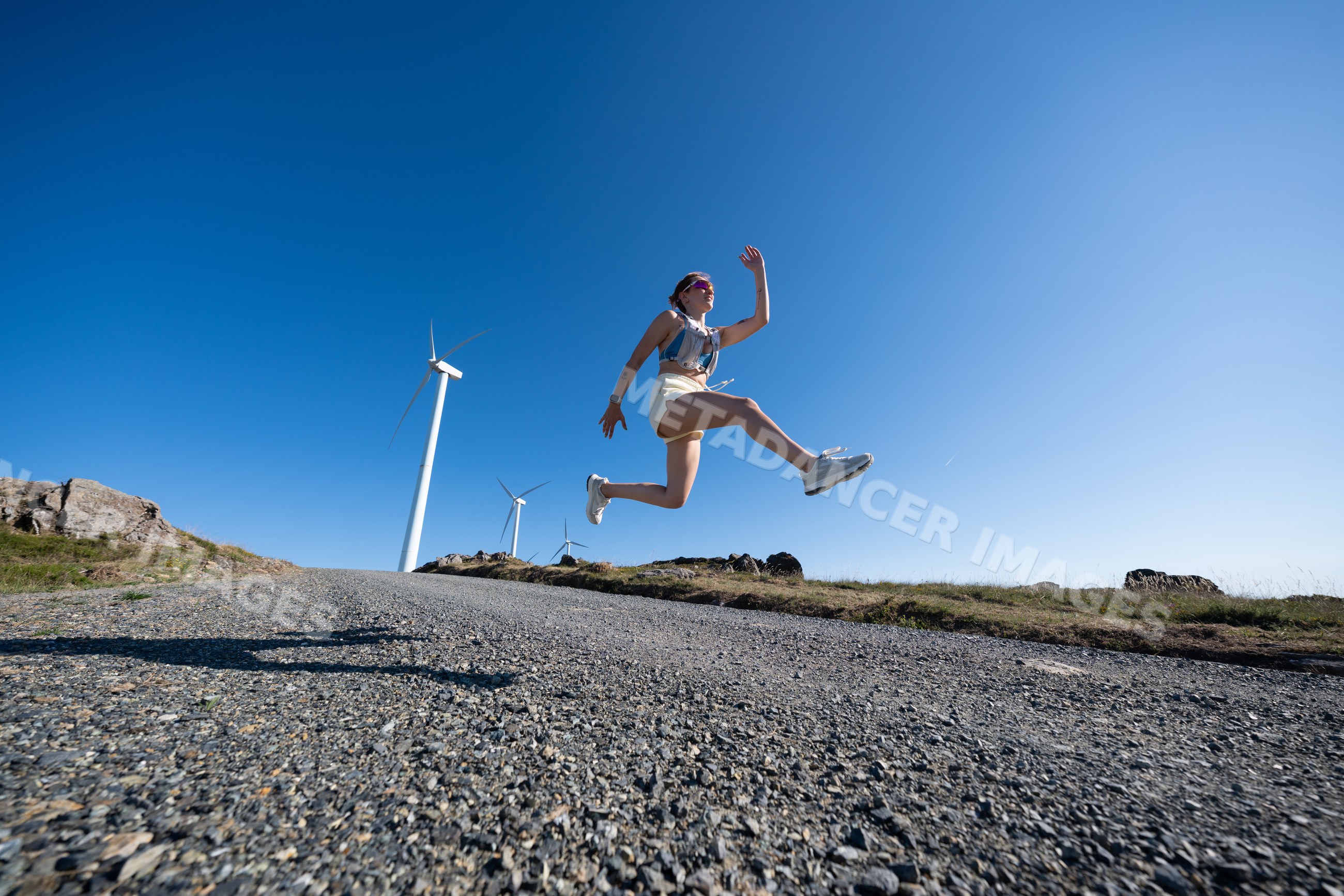 Young white woman jumps outdoors near wind turbines in Galicia, Spain