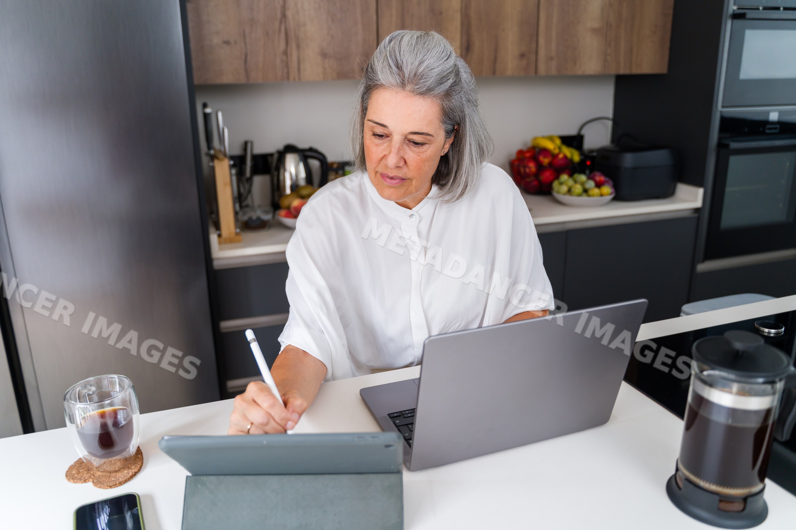 Older white woman multitasking with tablet and laptop