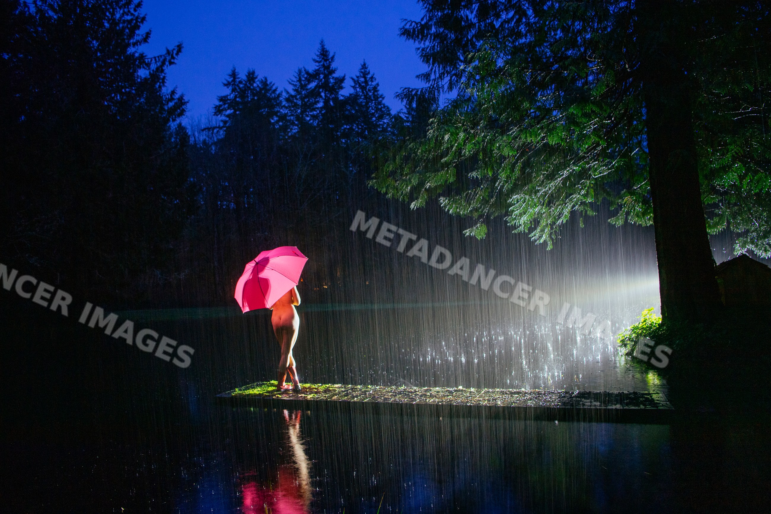 Nude white woman with pink umbrella in rain by lake at night