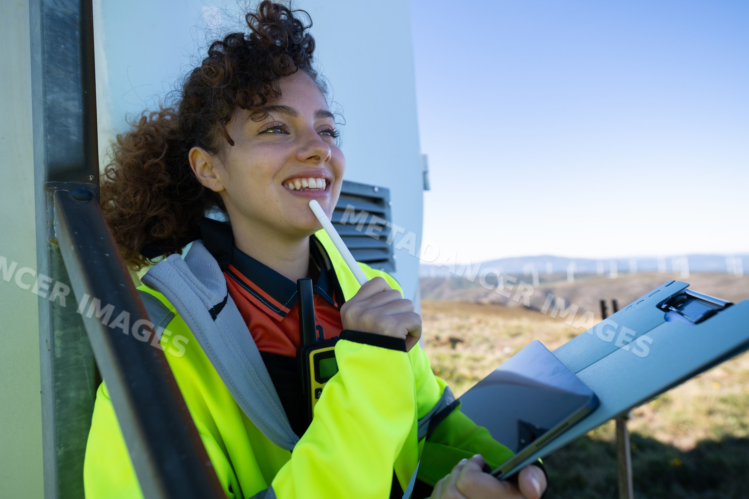 White woman holding clipboard and tablet at a wind turbine wind farm