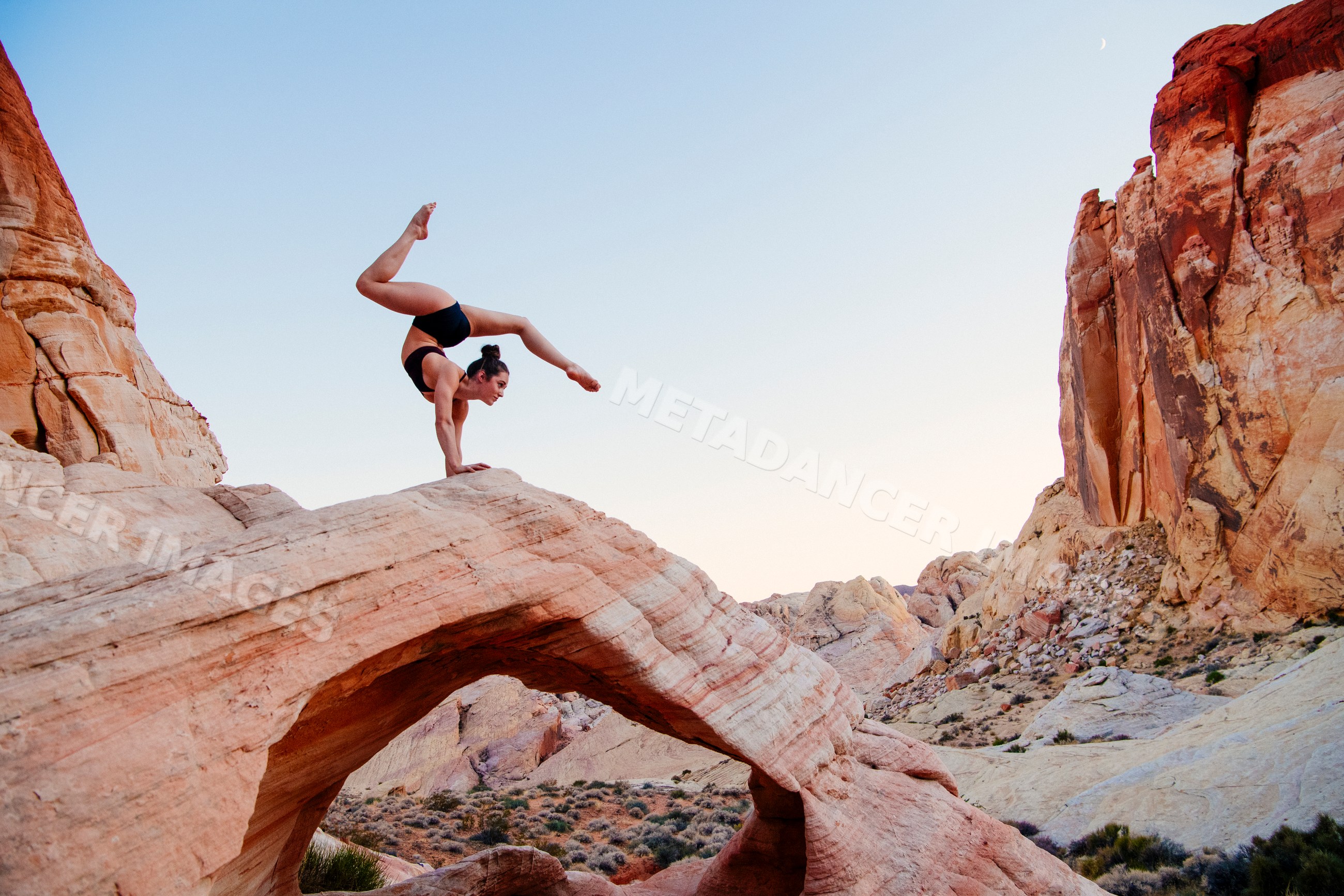 White woman practicing yoga handstand on natural arch rock in desert