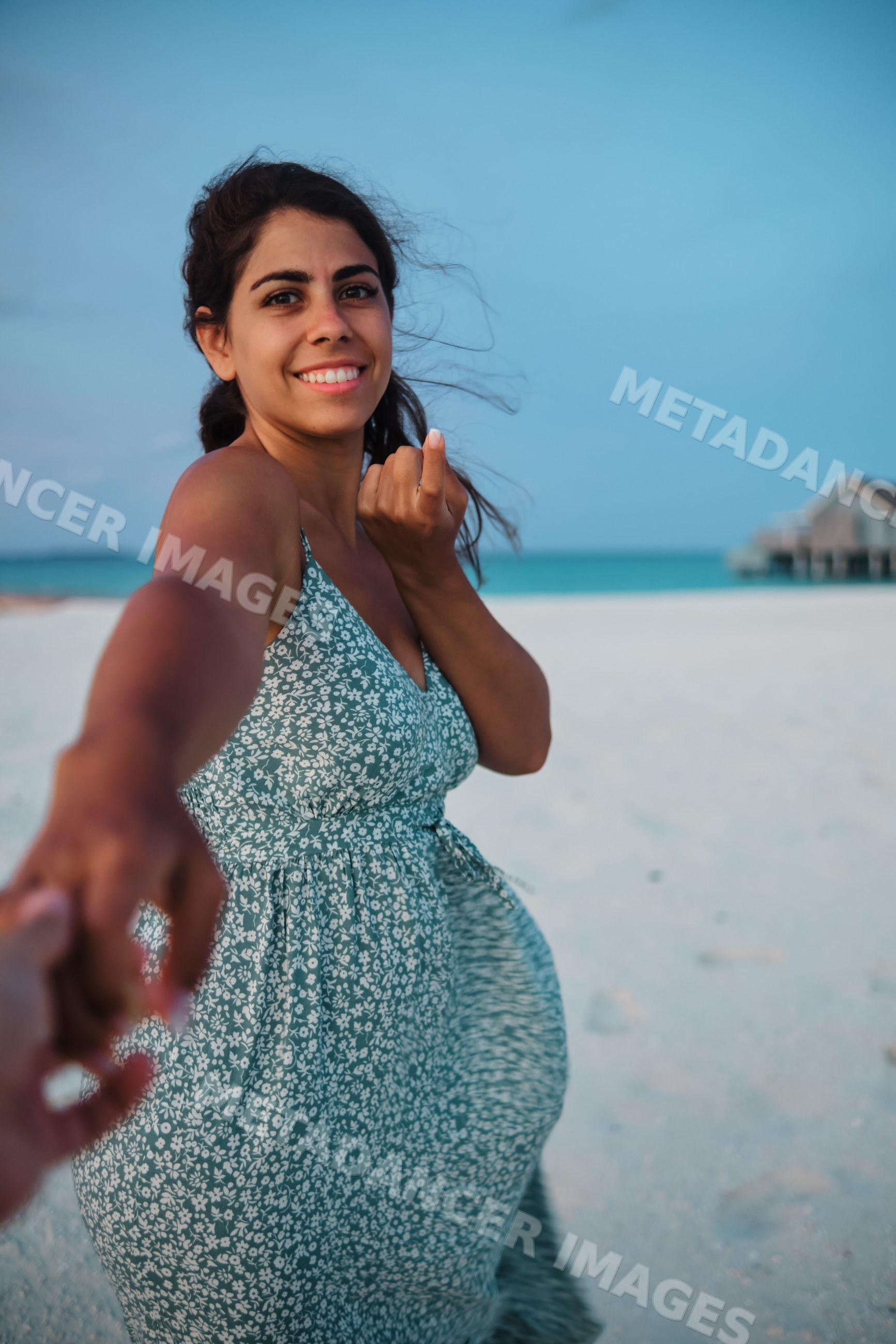A smiling white woman holds hands and walks on a beach in a beach