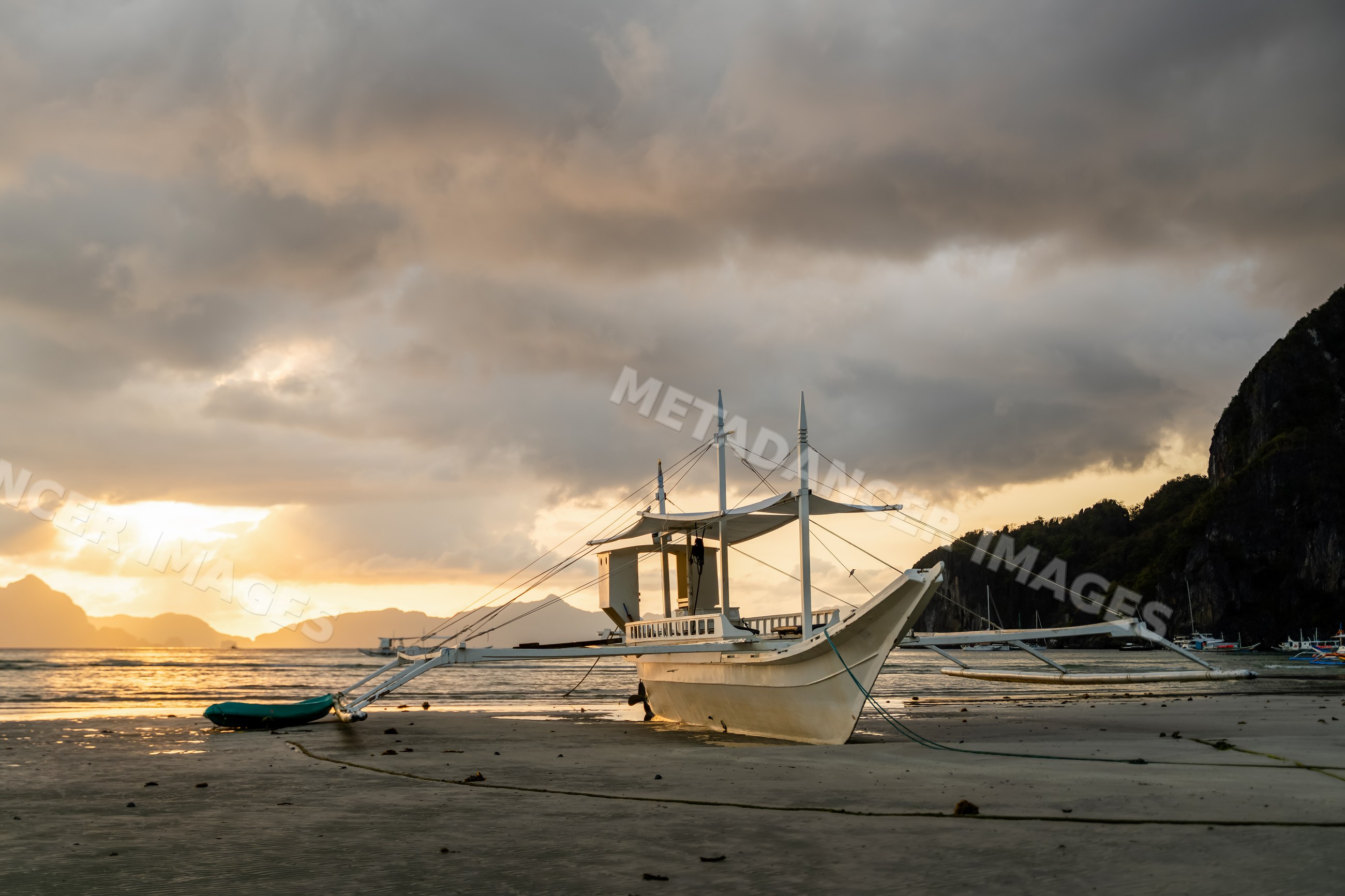 Outrigger boat anchored on sandy beach at sunset in the Philippines