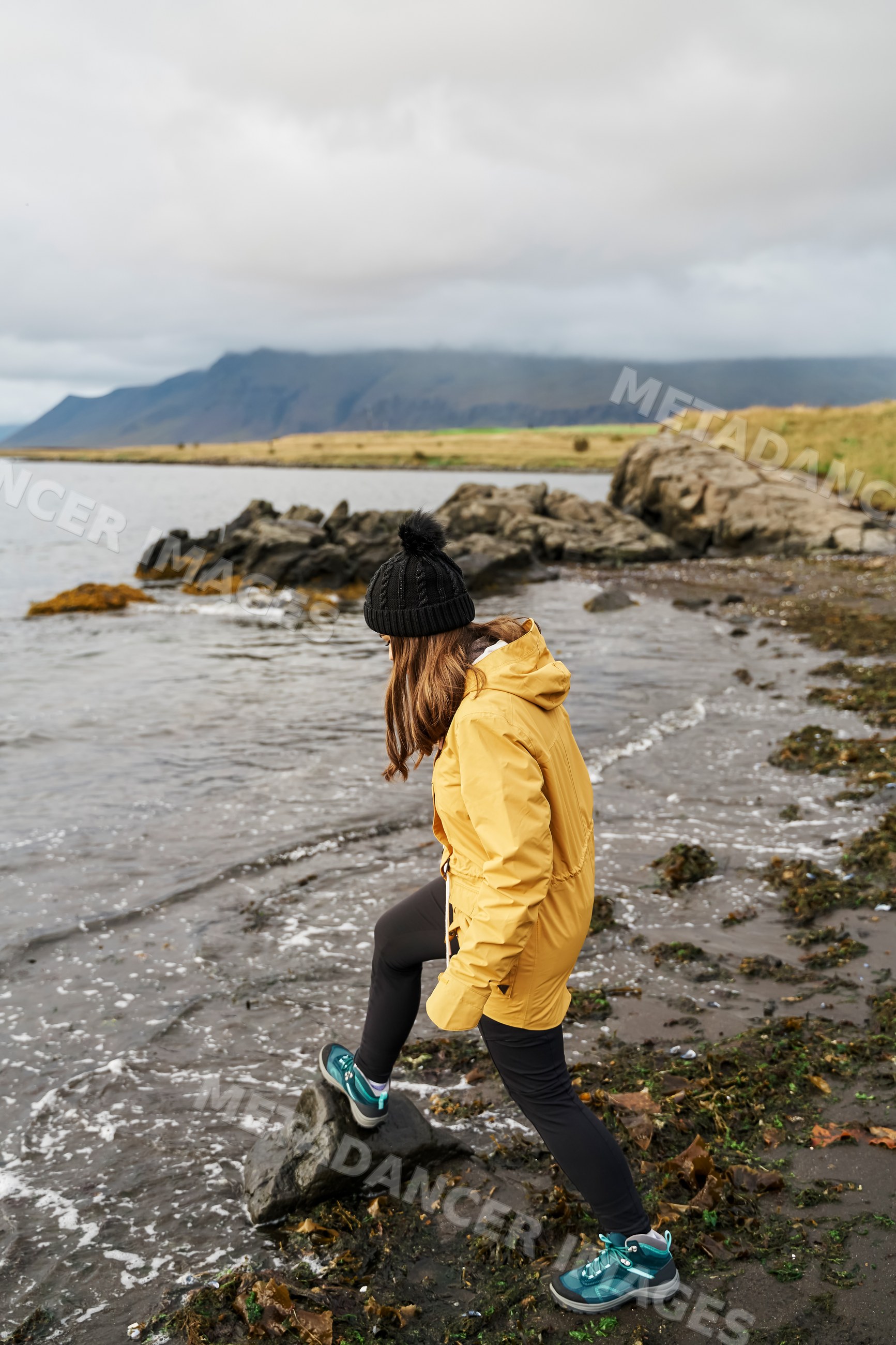 A white woman hikes on a rocky shore by the sea